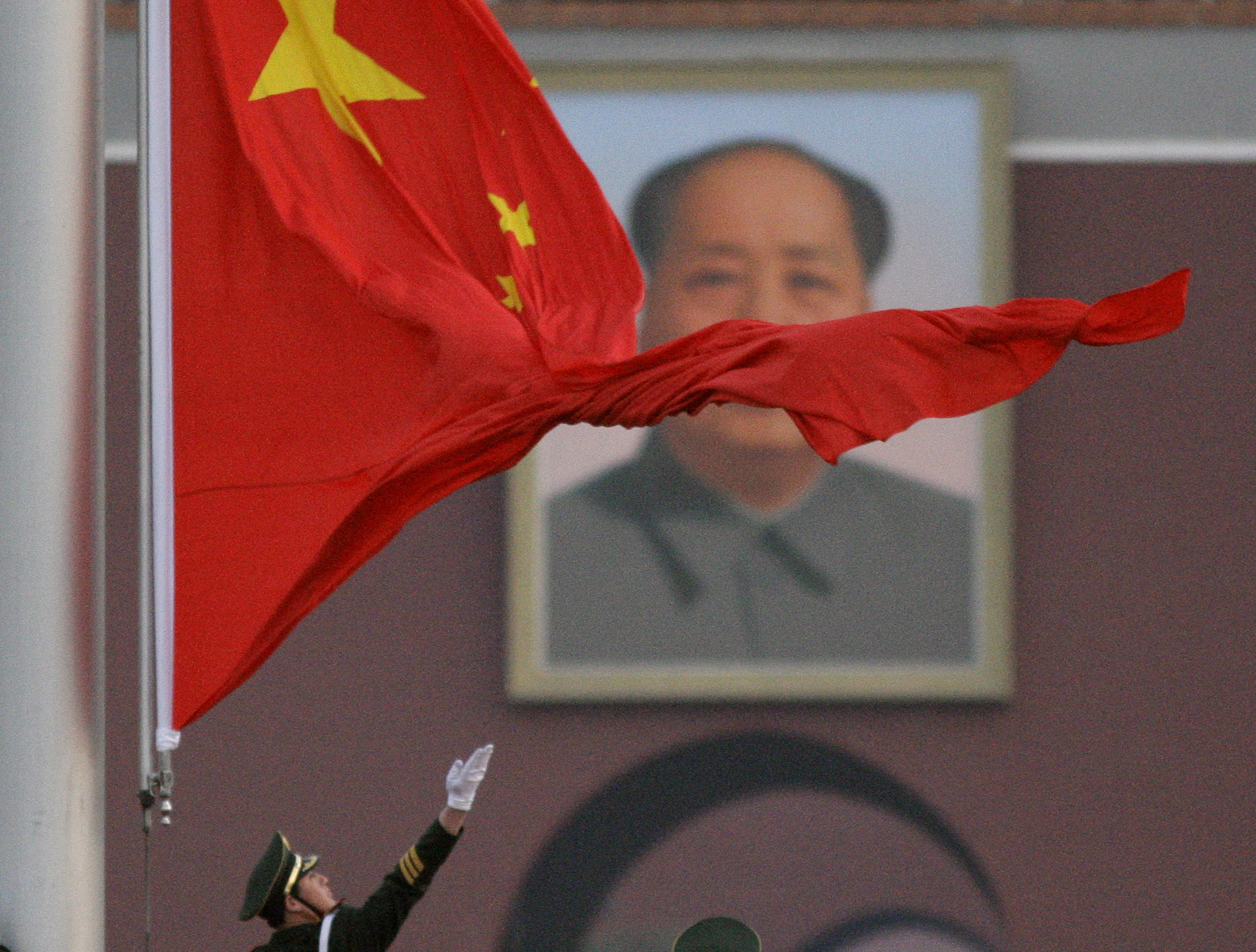 A paramilitary policeman throws the Chinese flag as he raises it in front of the portrait of Chairman Mao Zedong hanging in Beijing's Tiananmen Square March 5, 2008. REUTERS/David Gray     