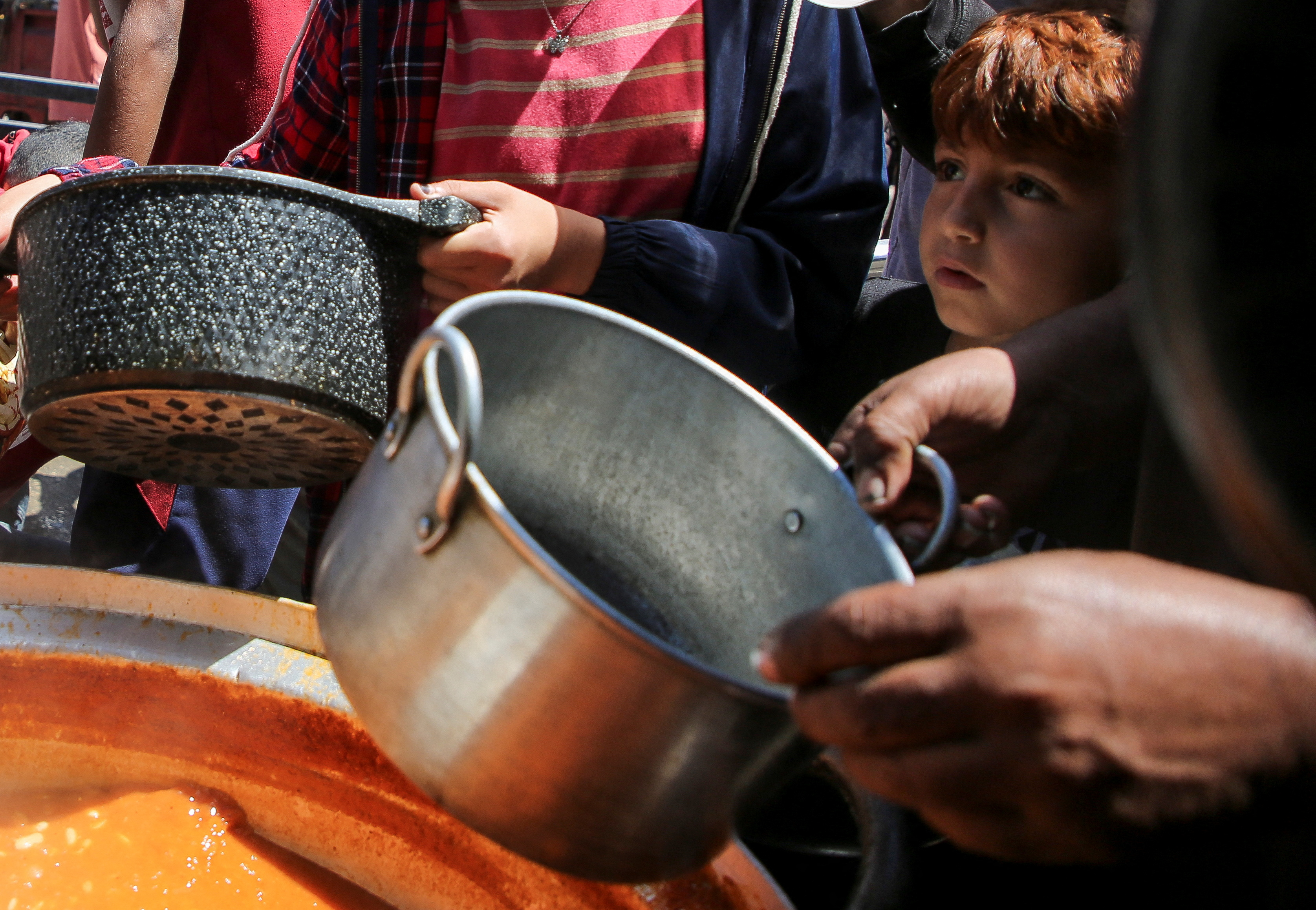Palestinians wait to receive food cooked by a charity kitchen, in Rafah, in the southern Gaza Strip