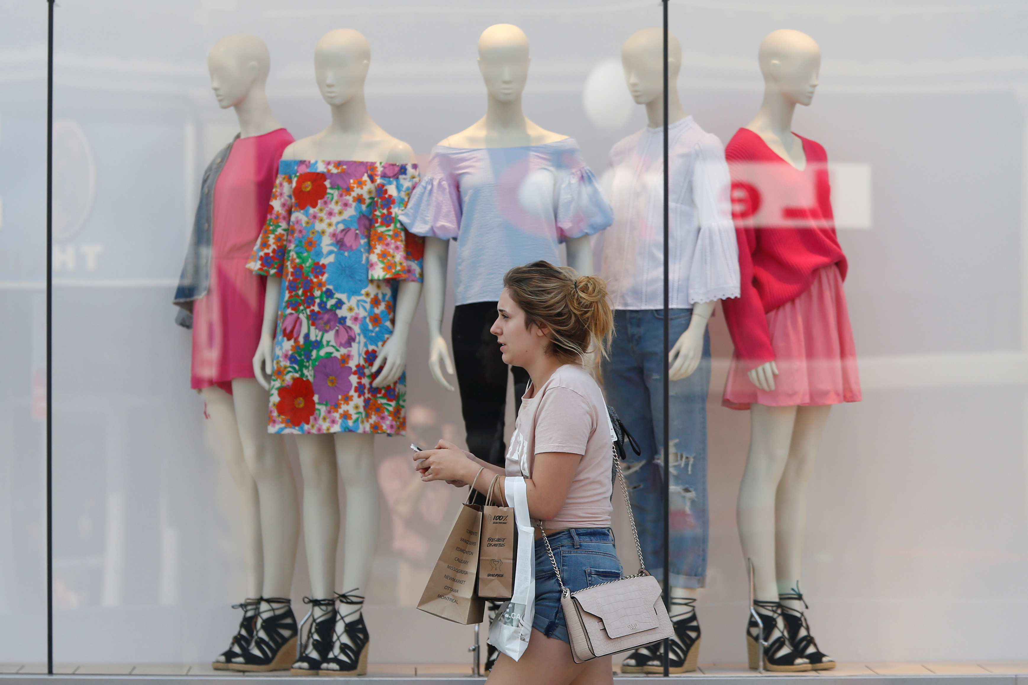 A woman carries shopping bags while walking past a window display outside a retail store in Ottawa