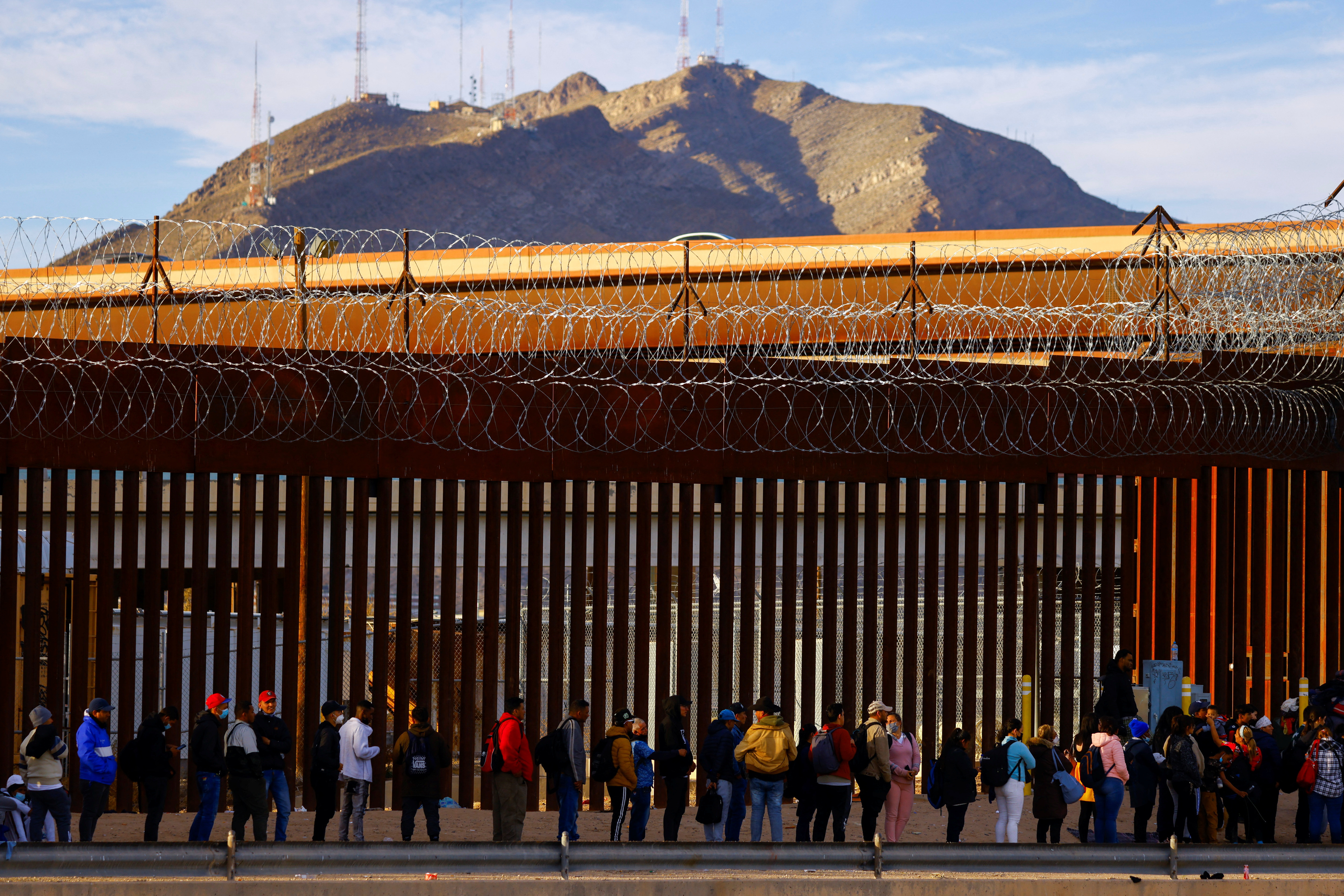 Migrants queue near the border fence, after crossing the Rio Bravo river, to request asylum in El Paso