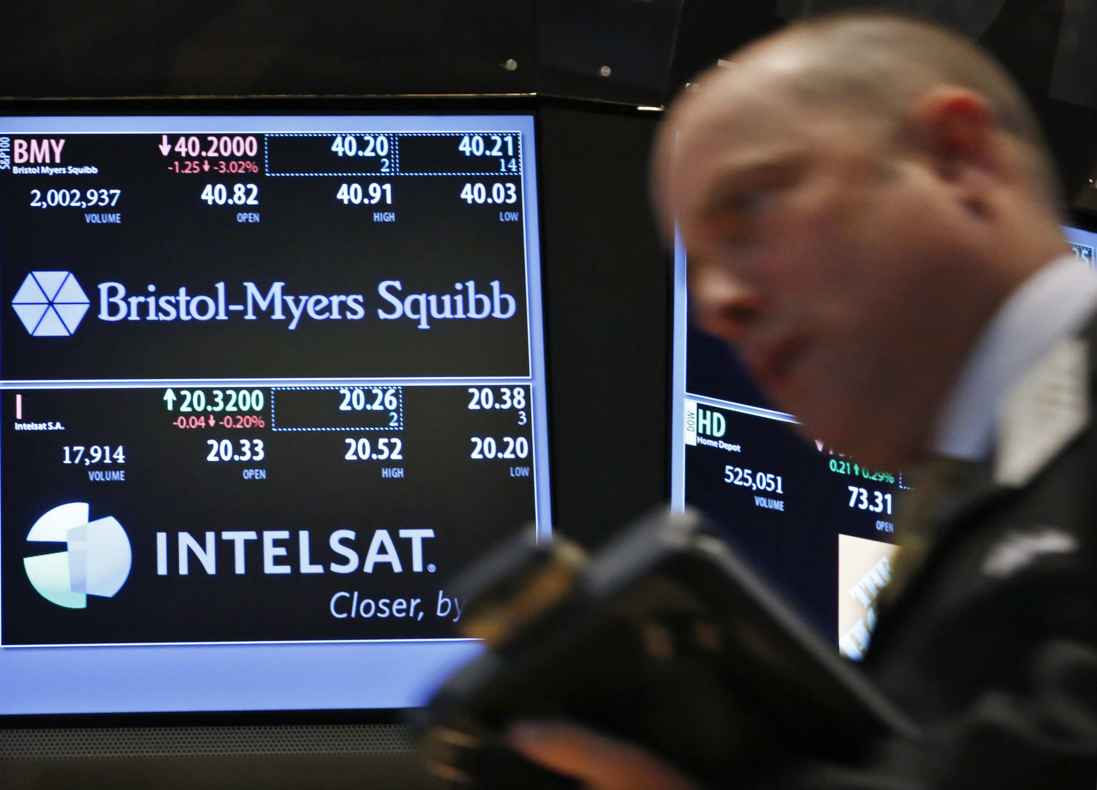 A trader passes by a screen displaying the tickers symbols for Bristol-Myers Squibb and Intelsat, Ltd. on the floor at the New York Stock Exchange