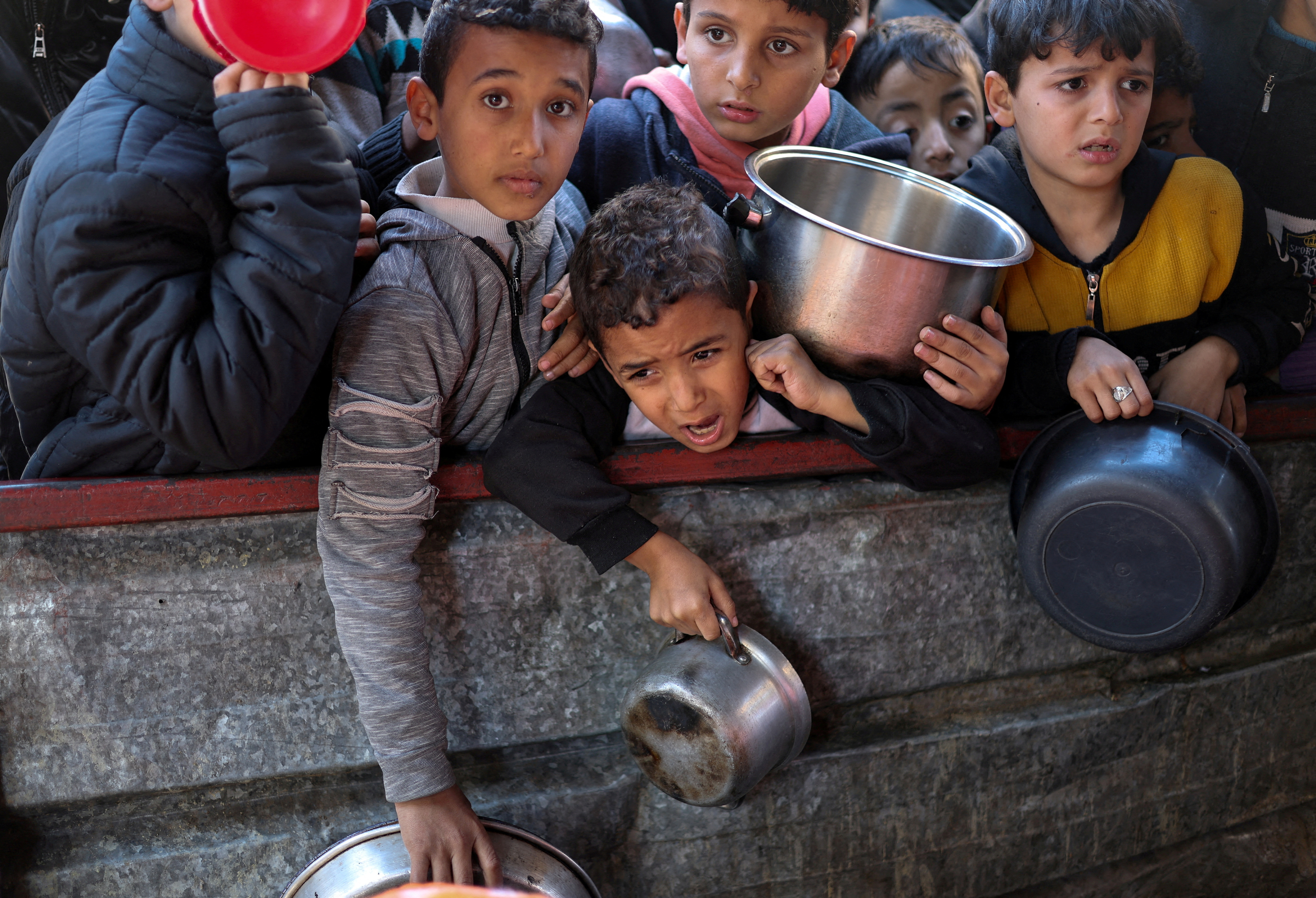 Palestinians wait to receive food cooked by a charity kitchen amid shortages, in Rafah
