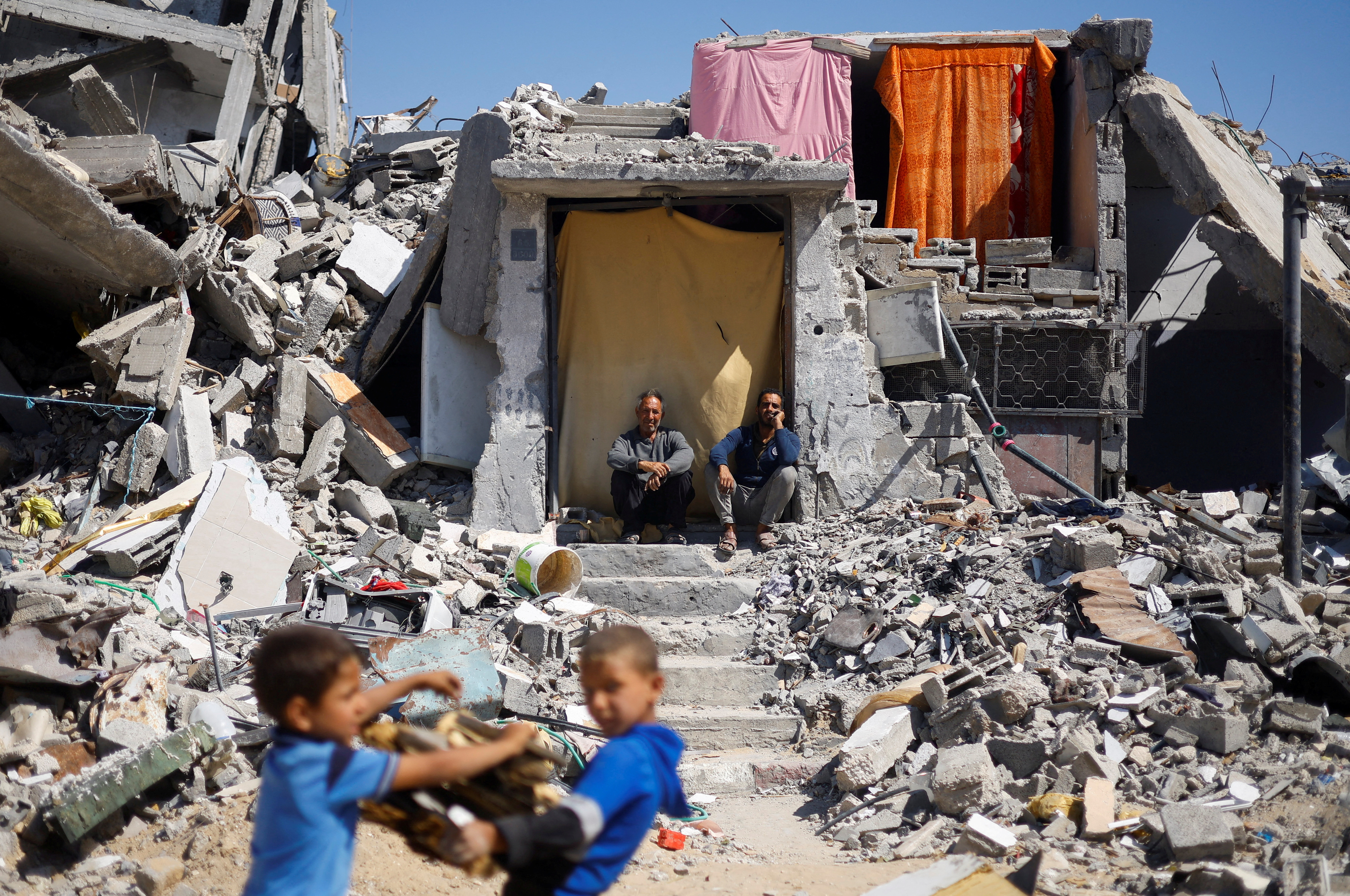 Palestinians sit at their house which was destroyed in an Israeli strike, amid the ongoing conflict between Israel and Hamas, in Khan Younis