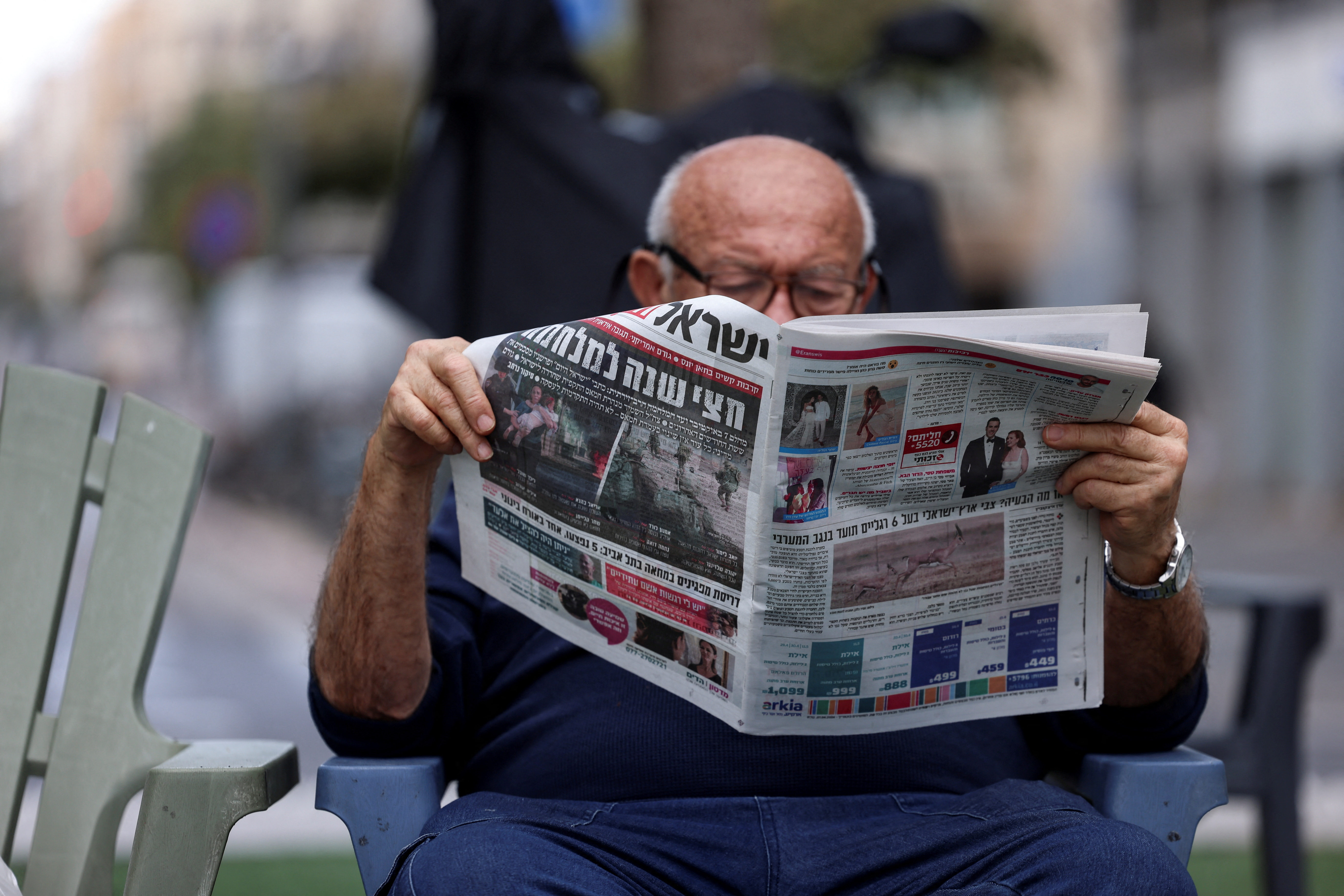 A man reads a newspaper with a headline on a page reading 