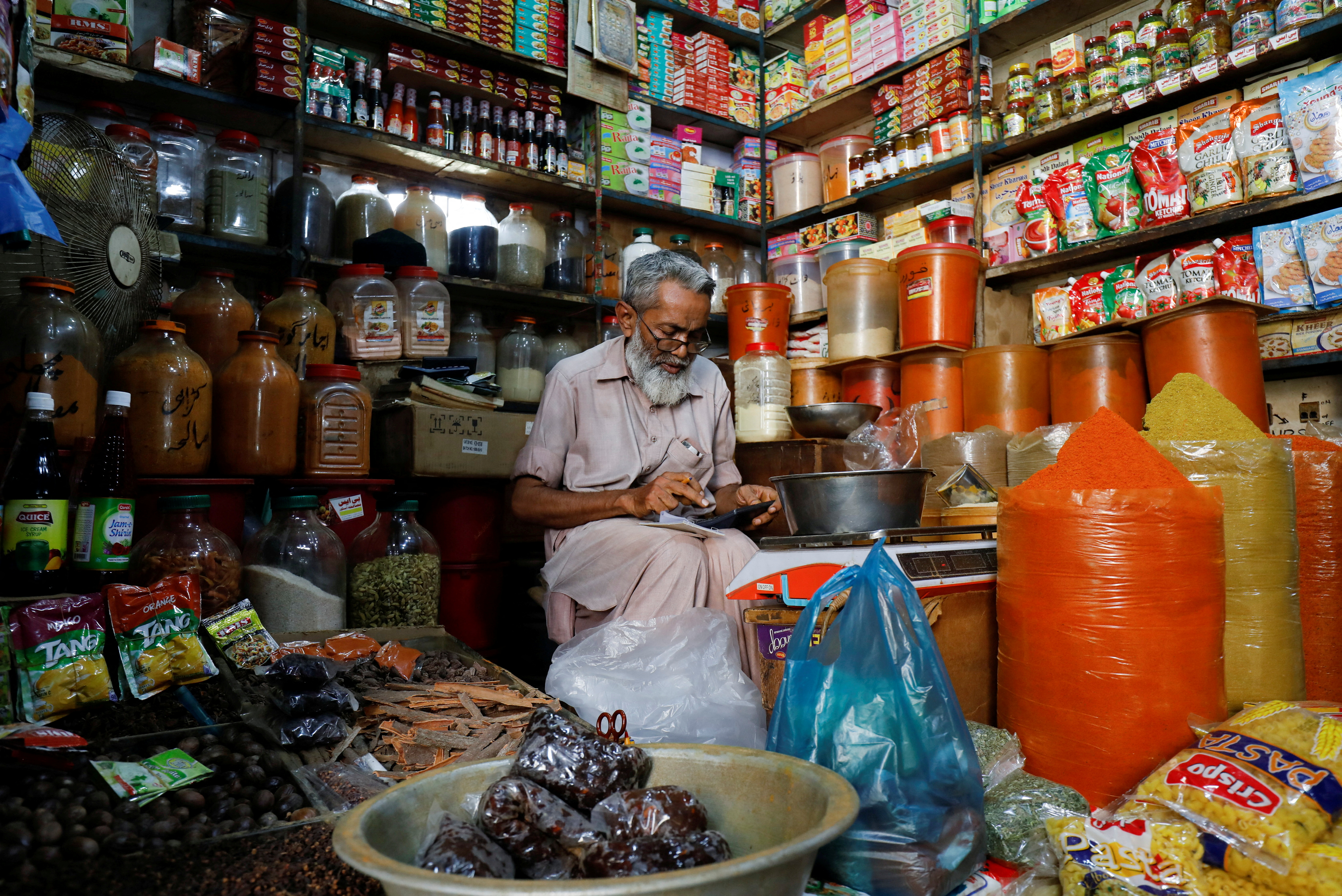Shopkeeper uses a calculator while selling spices and grocery items at a shop in Karachi