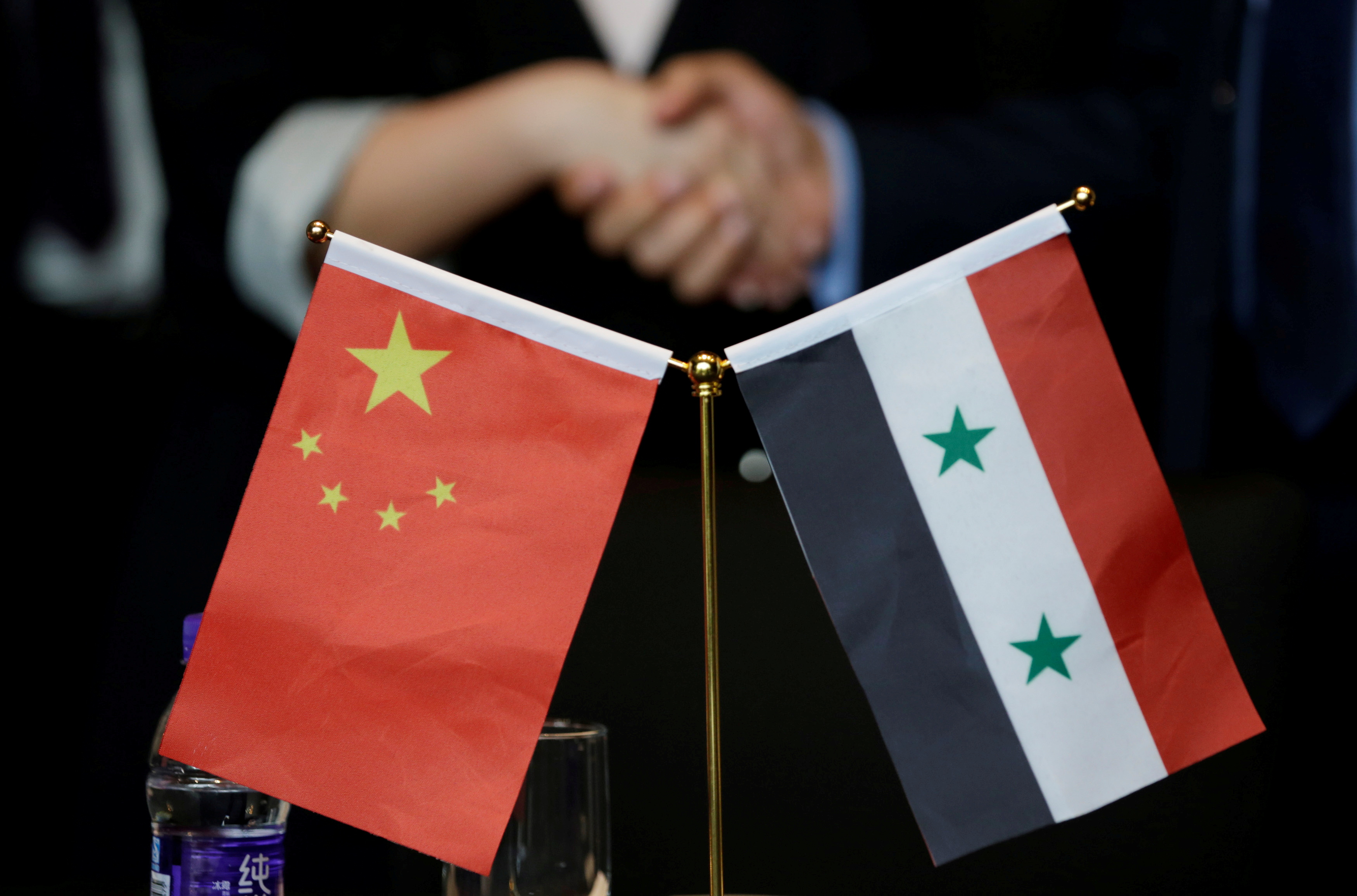 Chinese and Syrian businessmen shake hands behind their national flags in Beijing