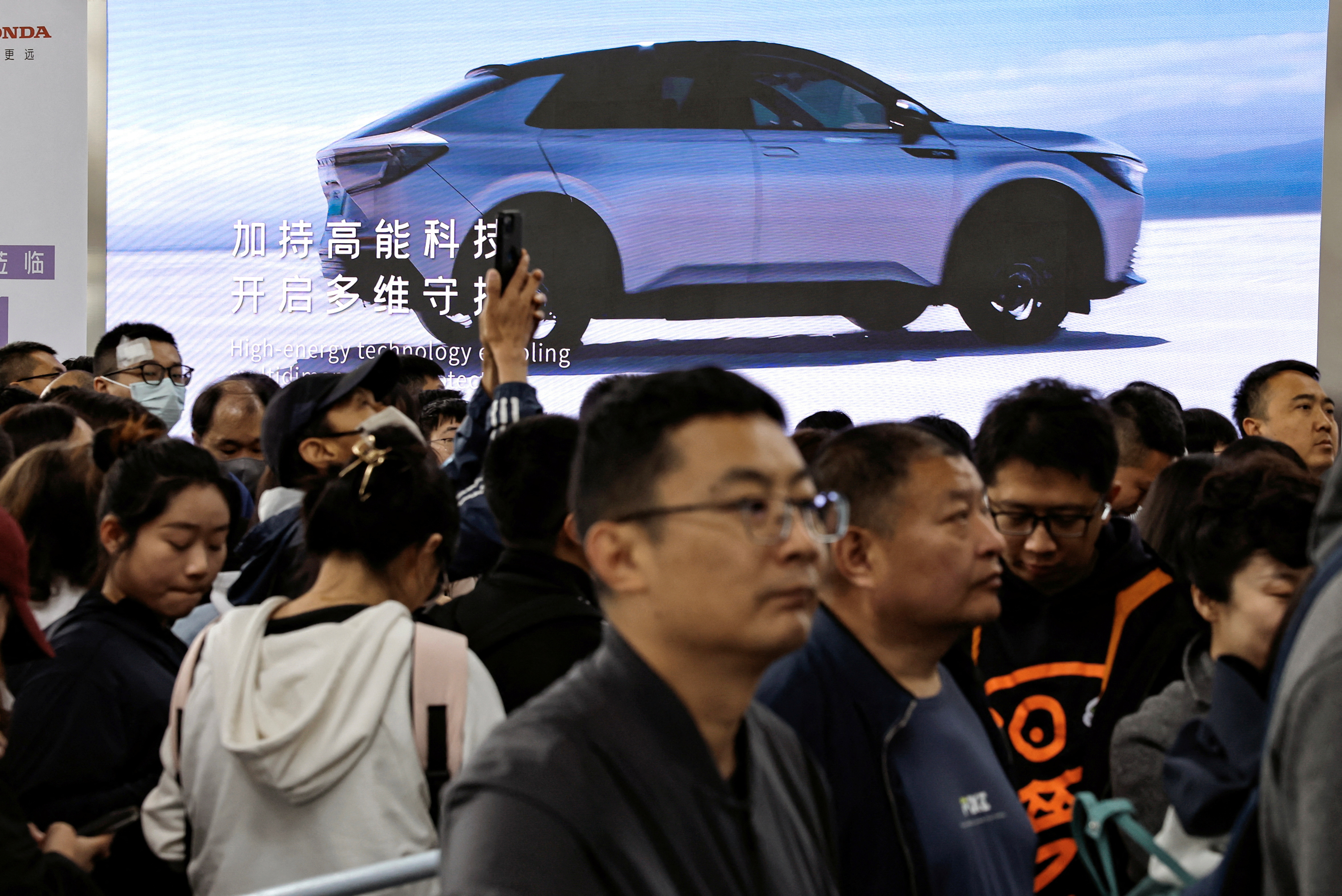 Visitors line up near a billboard of Honda's electric vehicle, at the Beijing International Automotive Exhibition