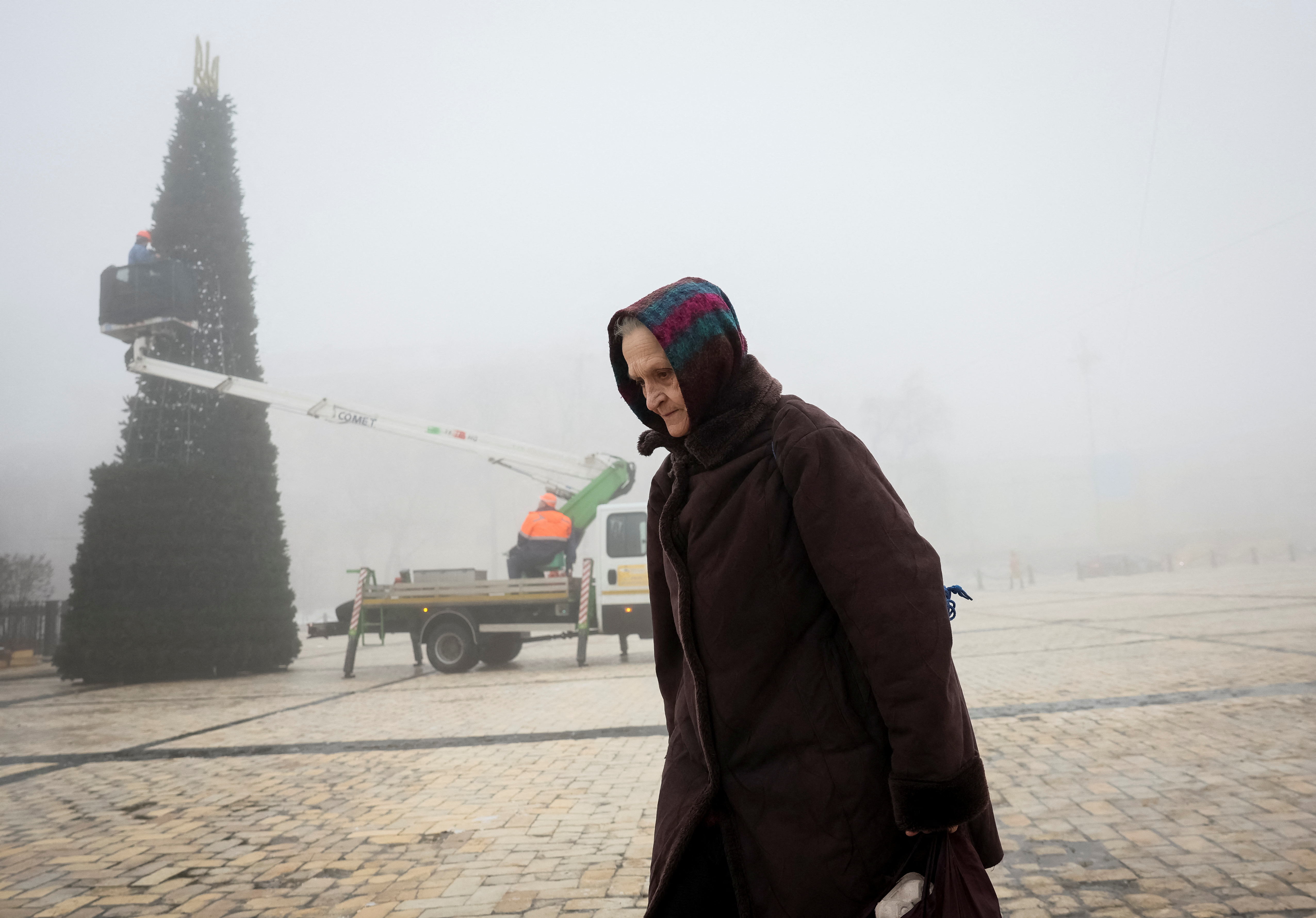 An old woman walks at the Sofiyska square as municipal workers install a Christmas tree during a heavy fog in Kyiv