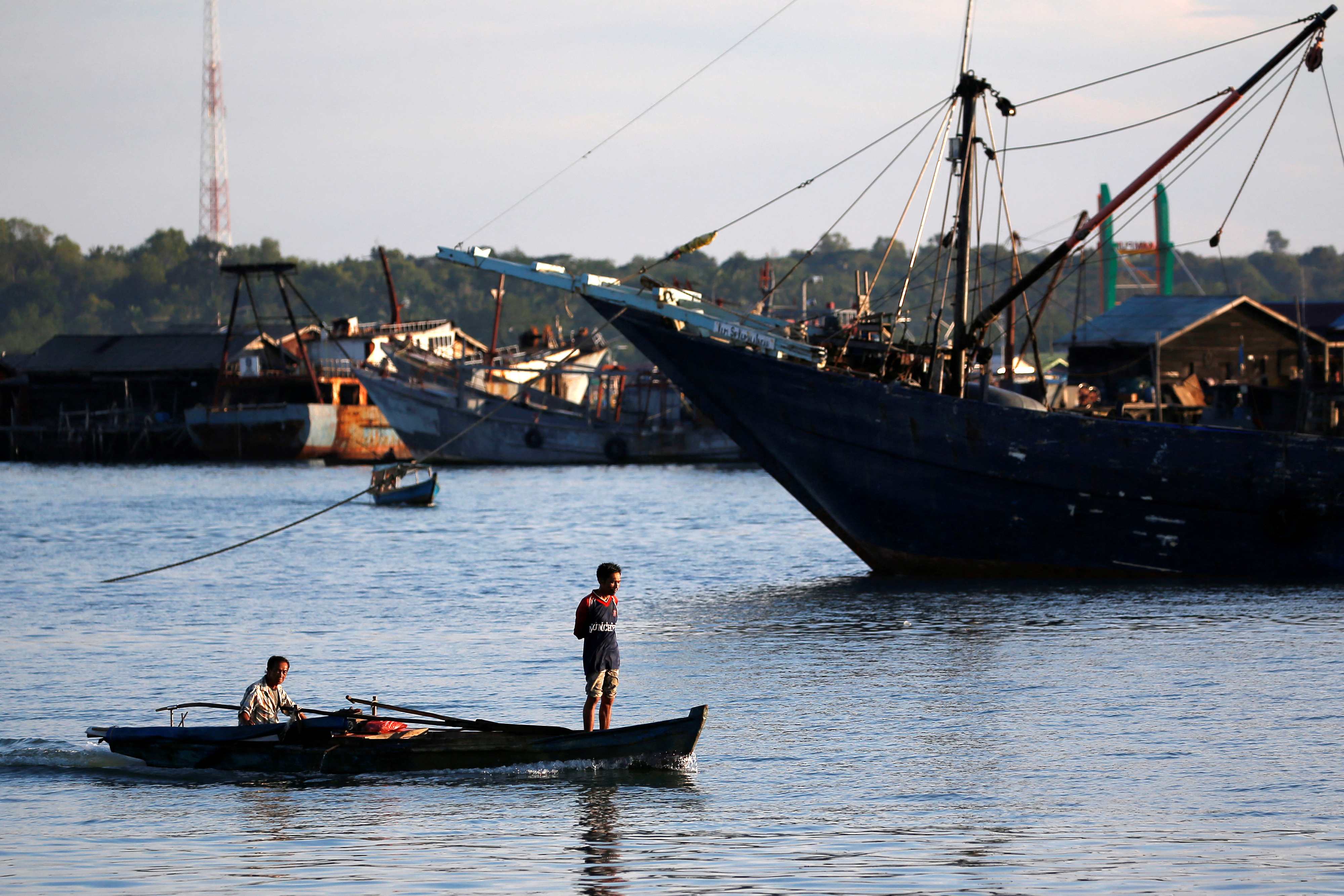 A man stands as he travels on a wooden boat near a port in Tanjungpinang, on the island of Bintan