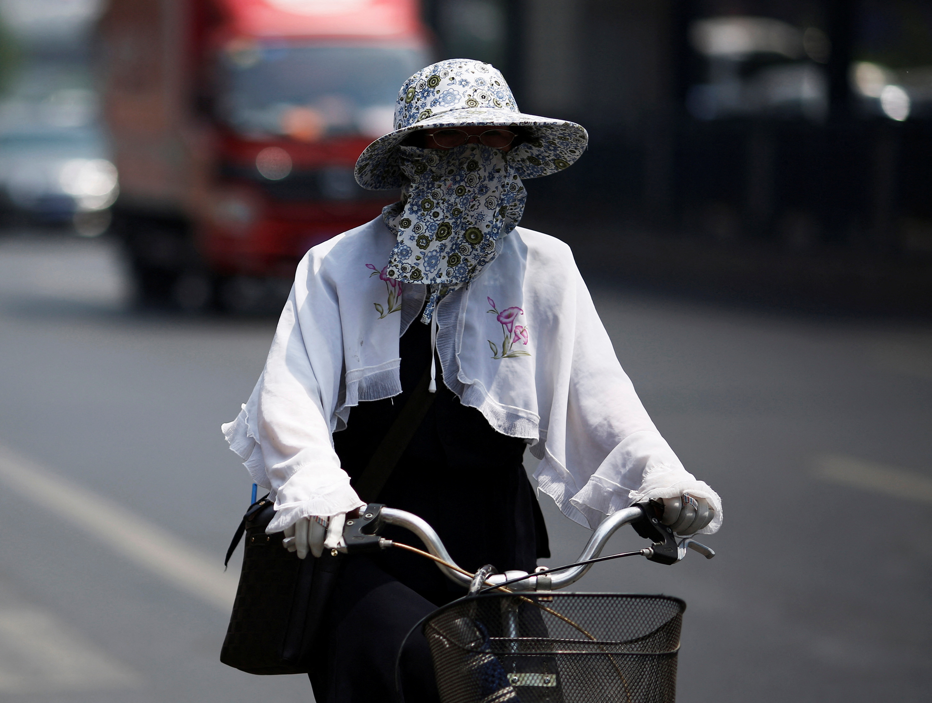 A woman covers herself with a hat and mask as she rides a bicycle in Beijing