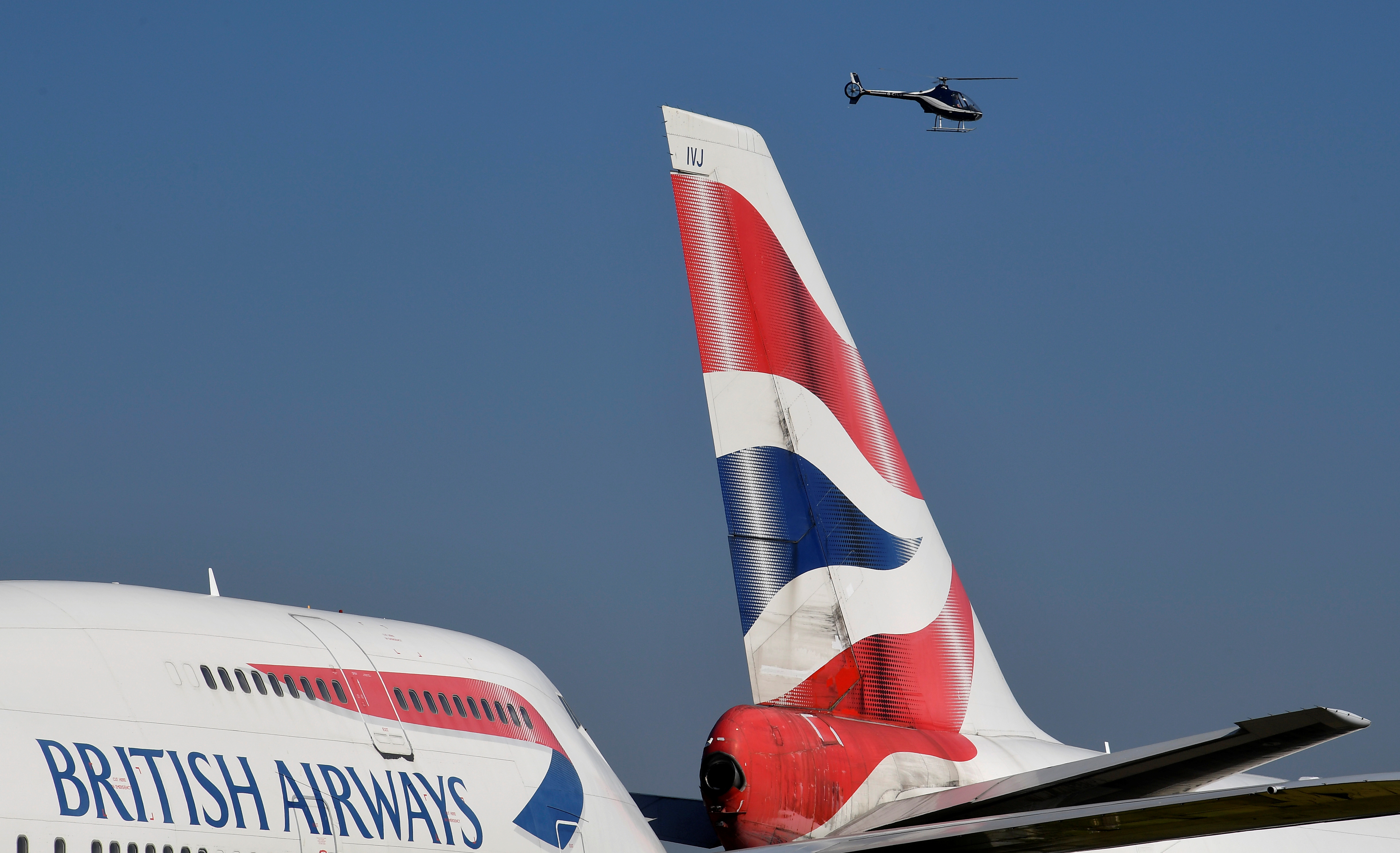 A helicopter flies near British Airways Boeing 747 jumbo jets parked to be used for salvage and parts after the airline retired its whole 747 fleet, amongst the spread of the coronavirus disease (COVID-19) pandemic, Cotswold Airport, Kemble, Britain, April 23, 2021. REUTERS/Toby Melville