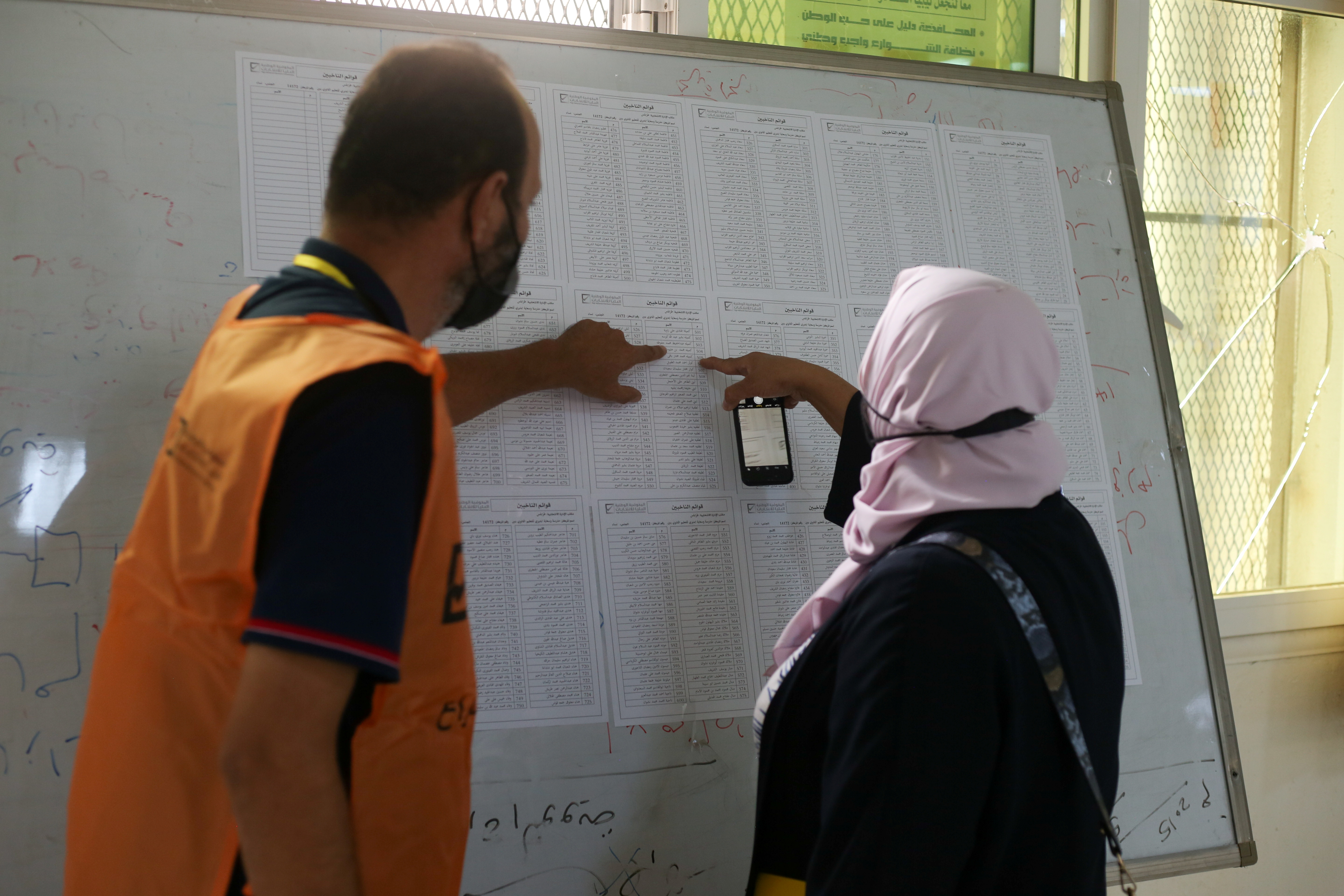 Woman is assisted as she checks names to receive her electoral card inside a polling station in Tripoli