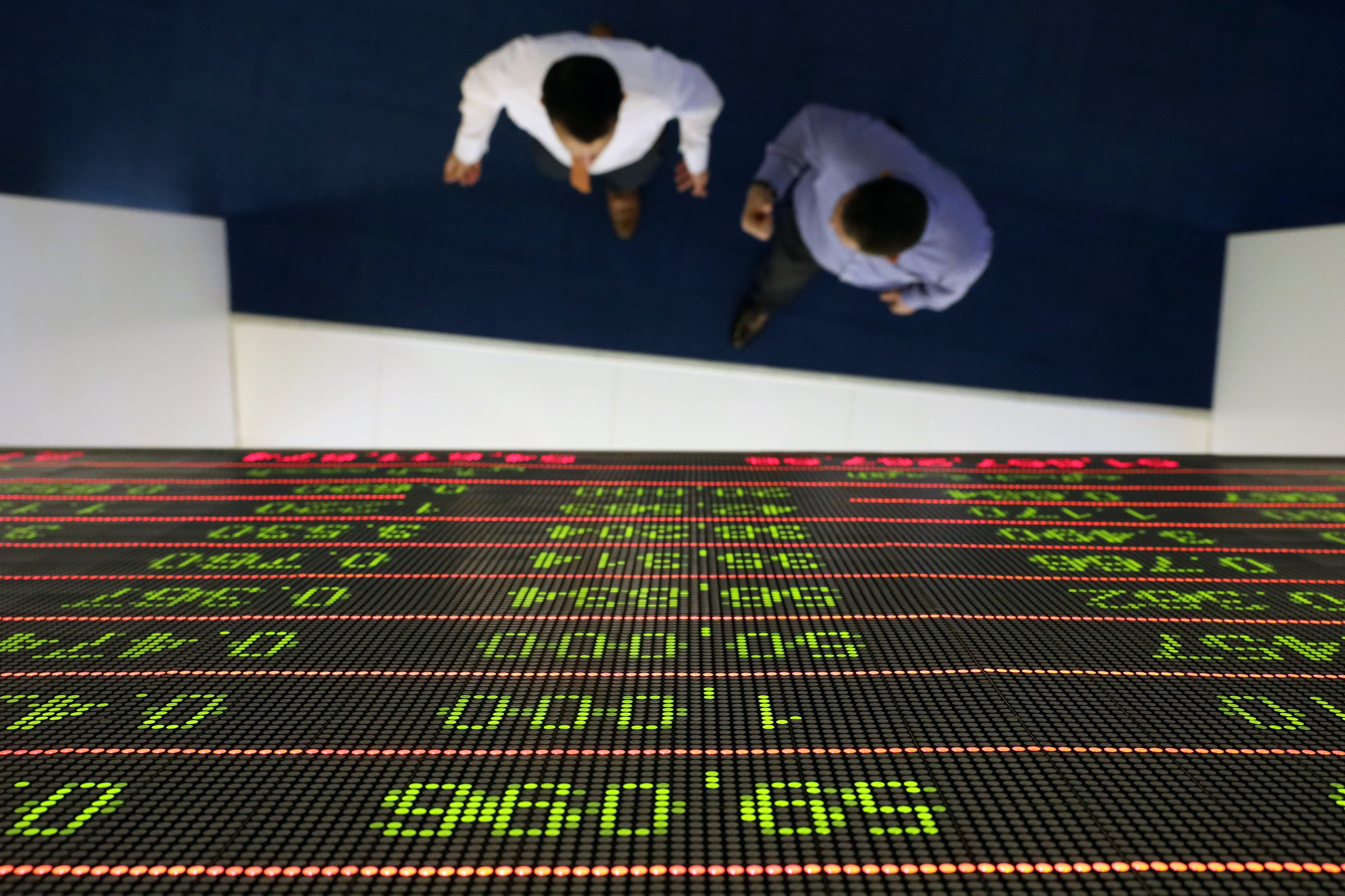 Investors walk under a stock index board at the Dubai Financial Market in Dubai