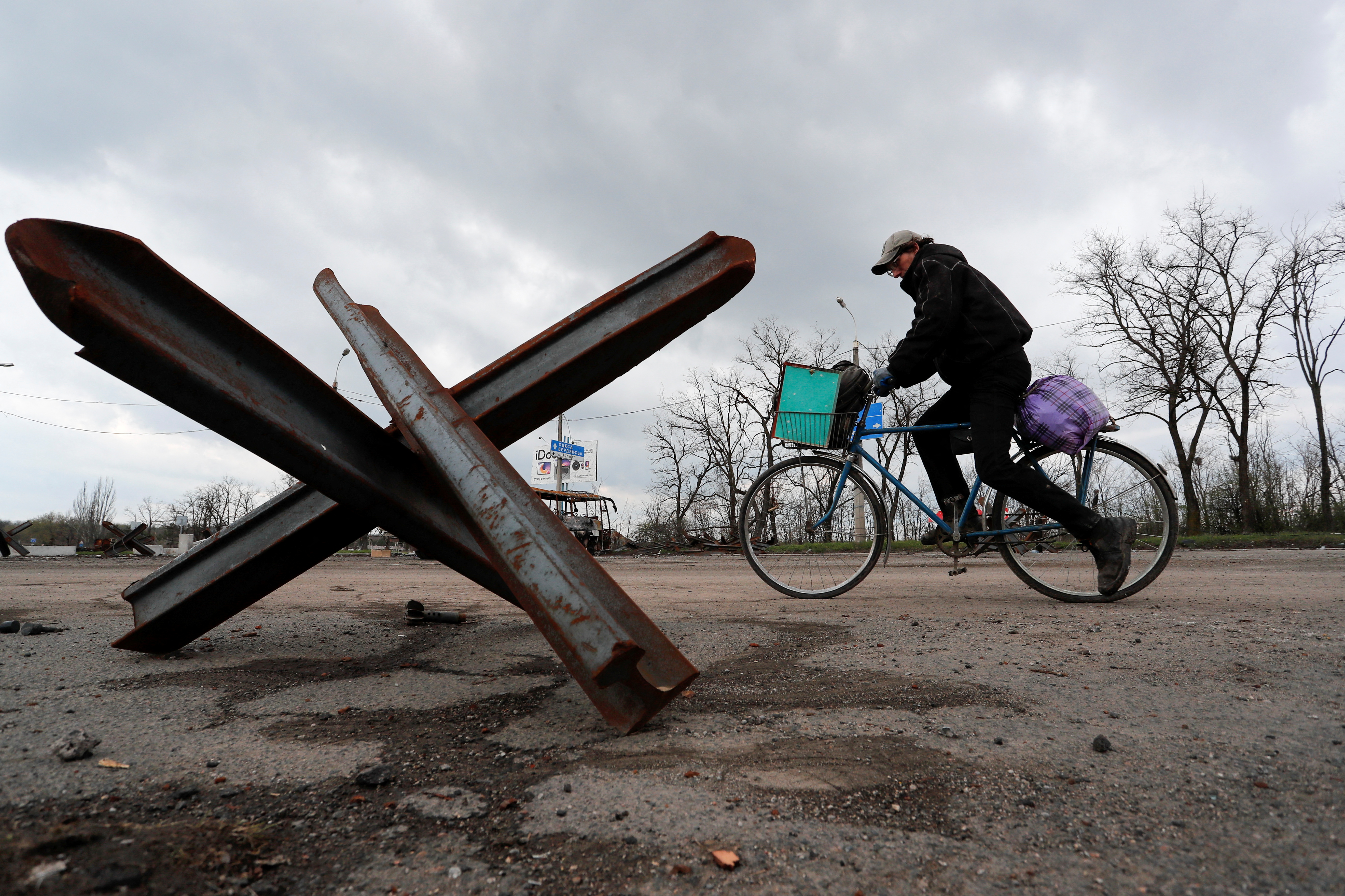 A man rides a bicycle near an anti-tank obstacle in Mariupol