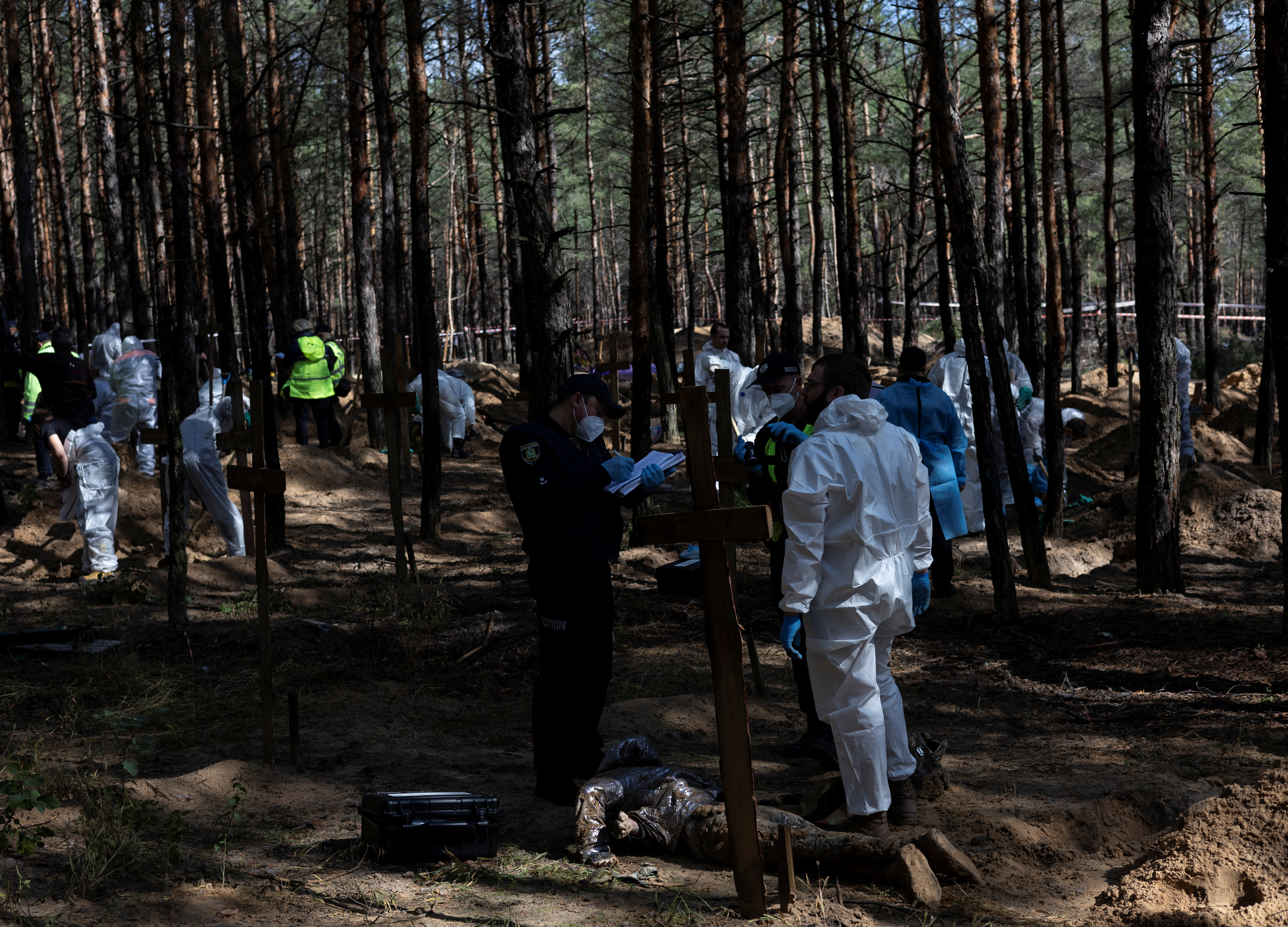 Experts work at a forest grave site during an exhumation in Izium