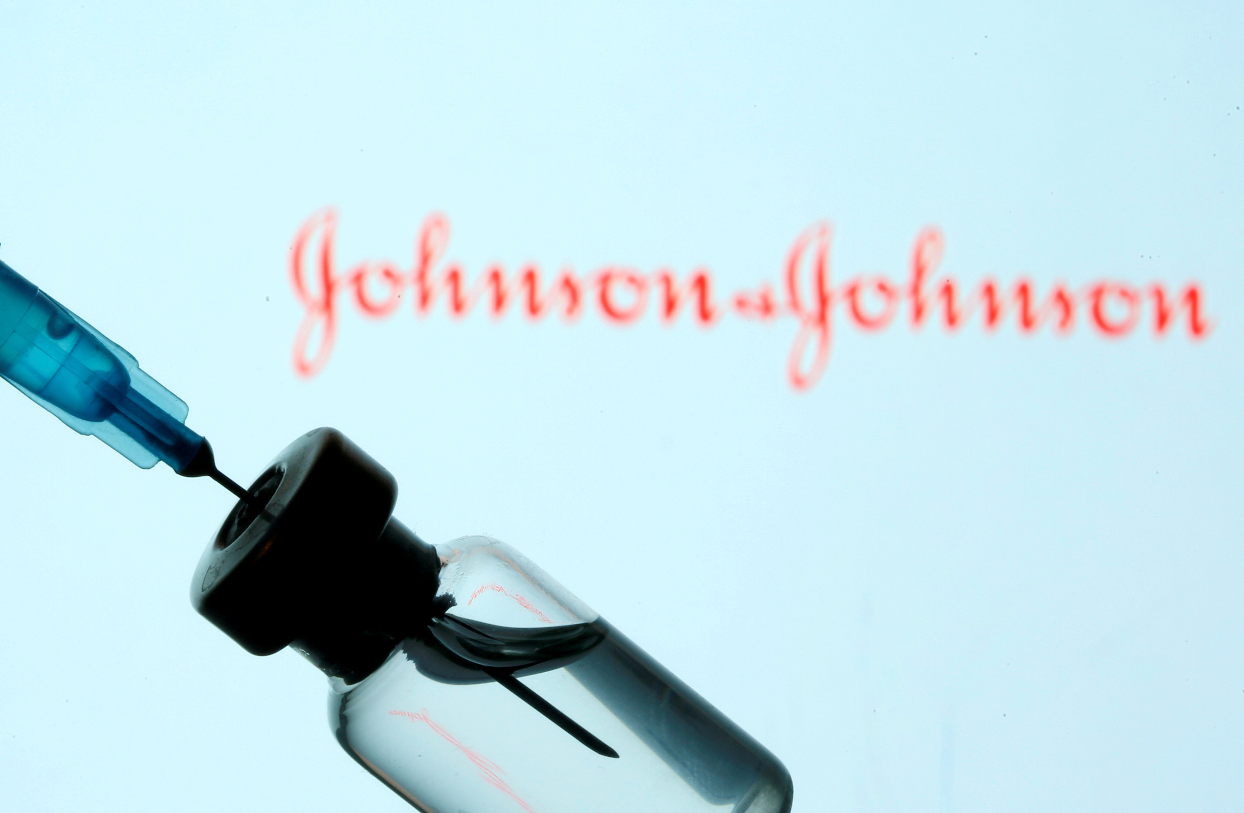 Vial and syringe are seen in front of displayed Johnson&Johnson logo in this illustration
