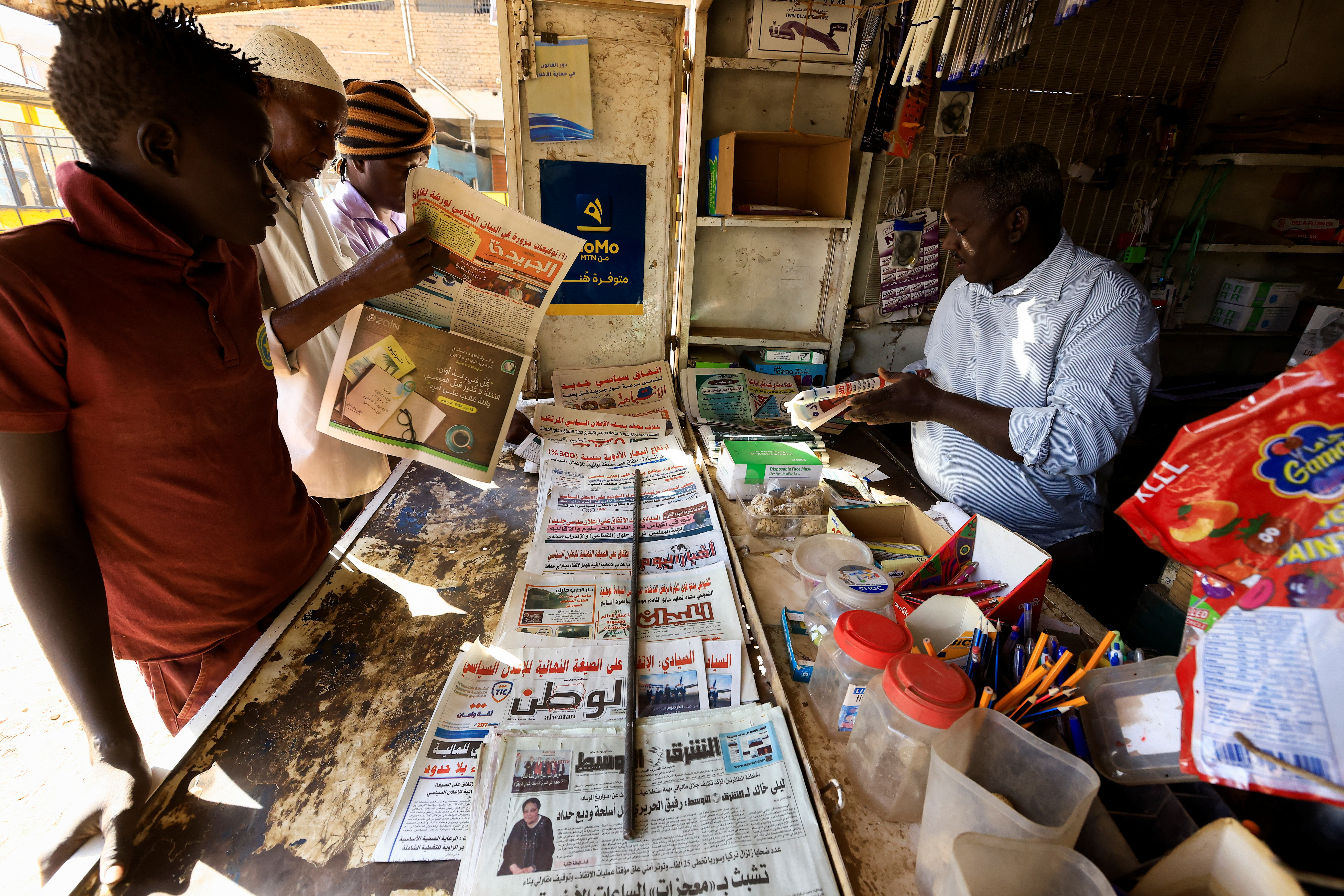 Owner of Al-Zikriyat library chats with people while he looks at newspapers in Omdurman