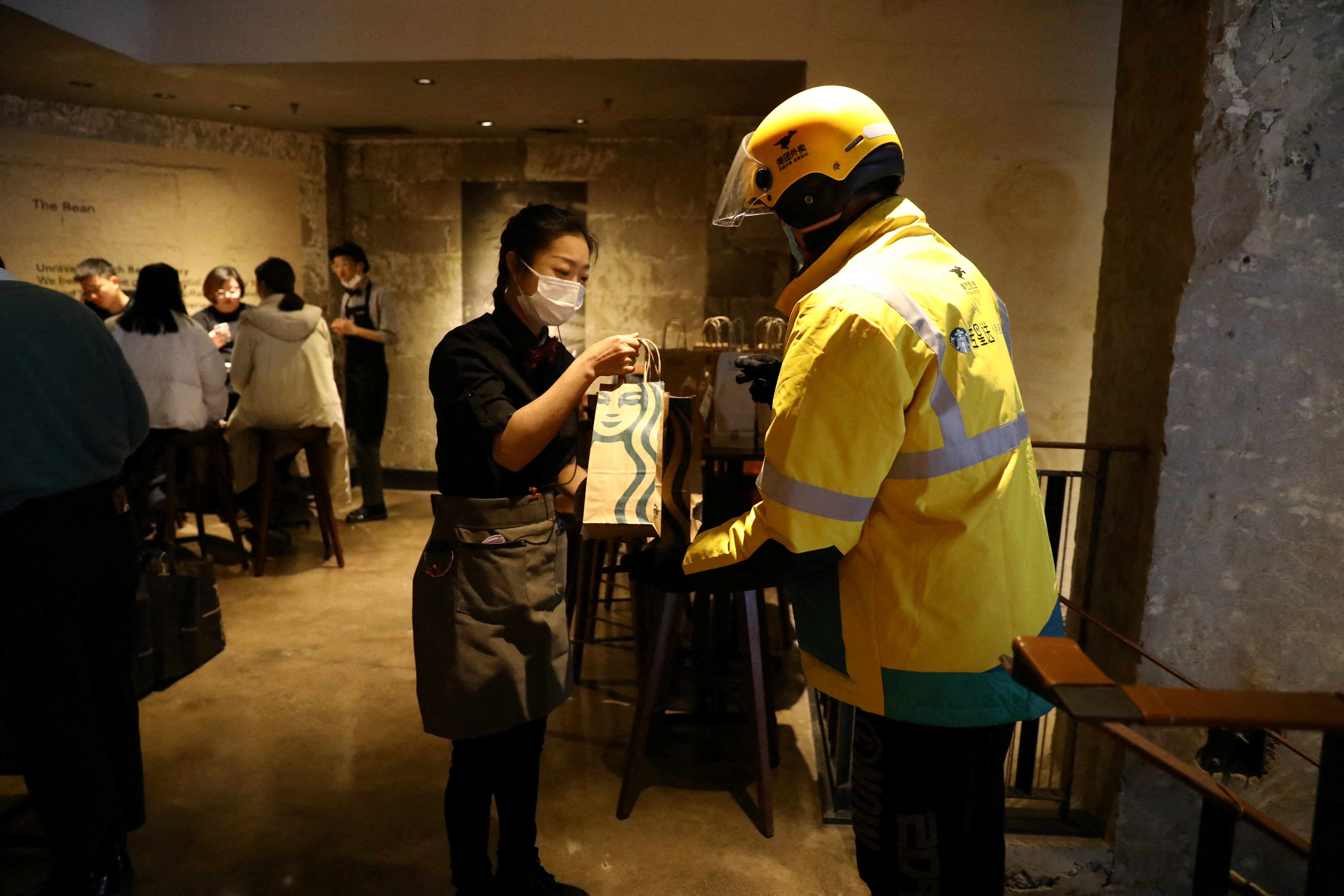 FILE PHOTO - A staff member takes a bag of ordered food from a Meituan delivery worker at a Starbucks flagship store in Beijing