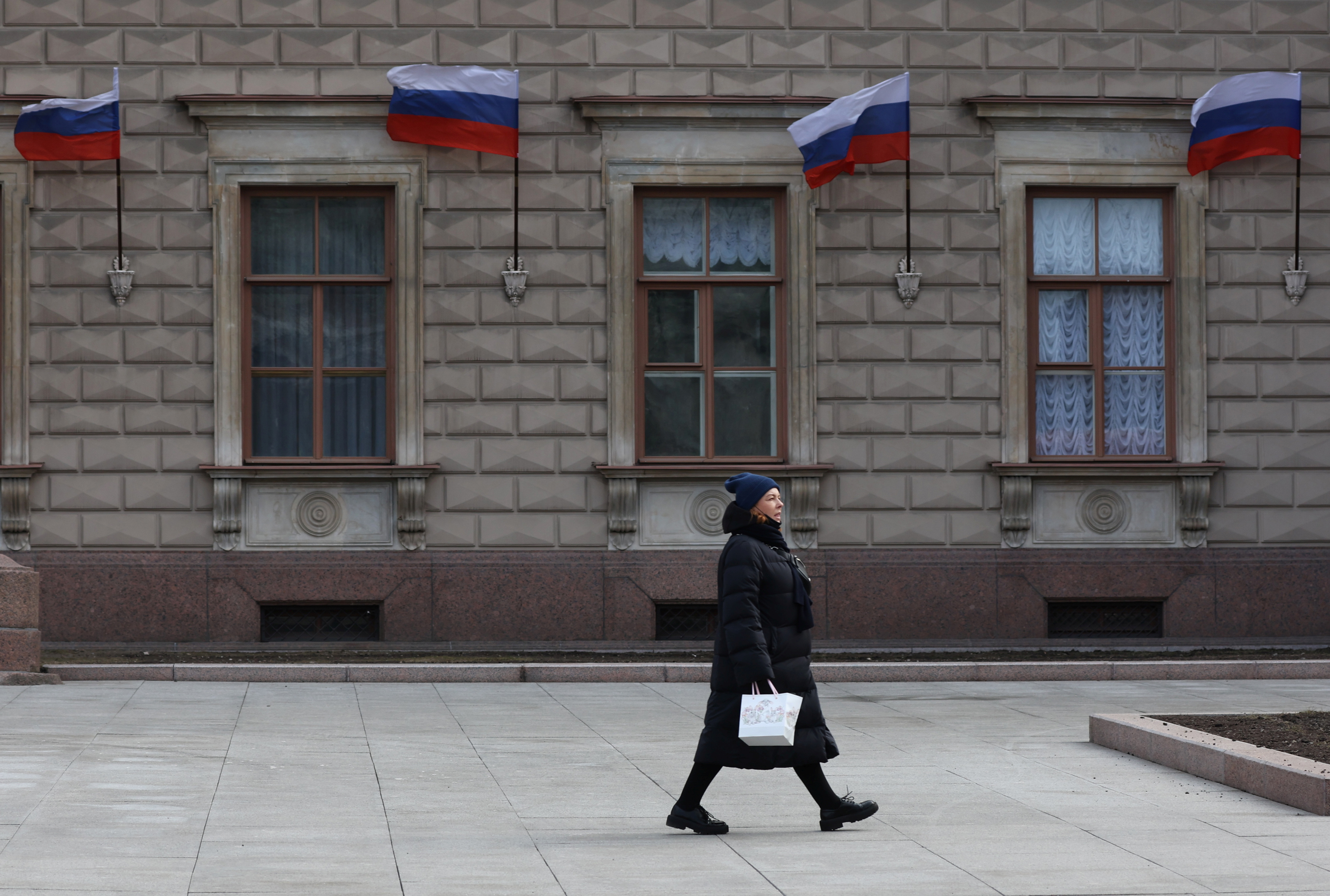 A woman walks past a building with Russian flags placed on its wall in Saint Petersburg