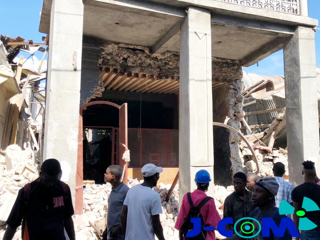 People stand in front of collapsed buildings following an earthquake in Jeremie, Haiti August 14, 2021, in this picture obtained from social media. Courtesy of TWITTER @JCOMHaiti/ via REUTERS ATTENTION EDITORS - THIS IMAGE HAS BEEN SUPPLIED BY A THIRD PARTY. MANDATORY CREDIT. MUST NOT OBSCURE LOGO