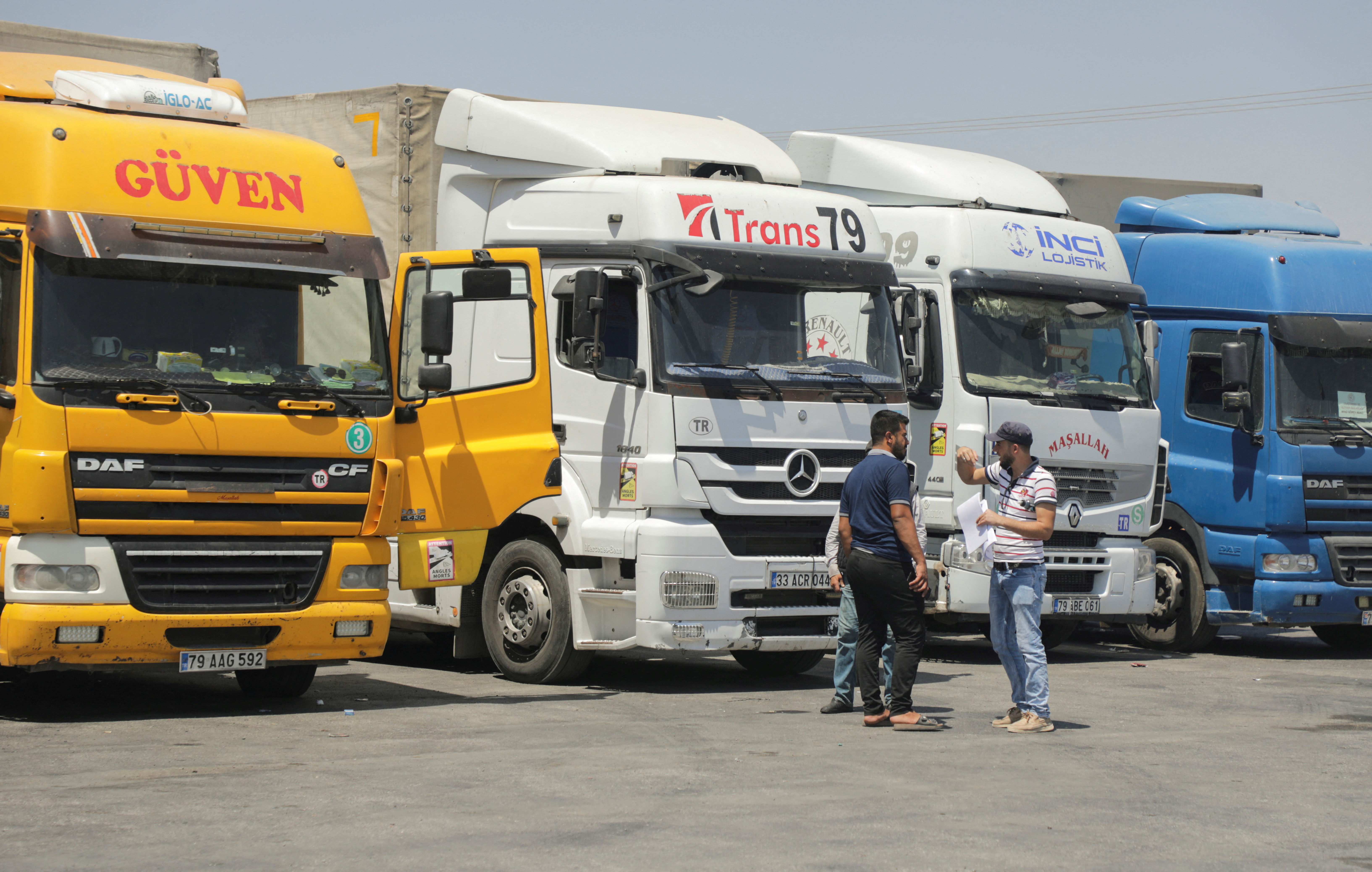 Halep kırsalındaki Bab al-Selama sınır kapısında park etmiş kamyonların yanında duran insanlar