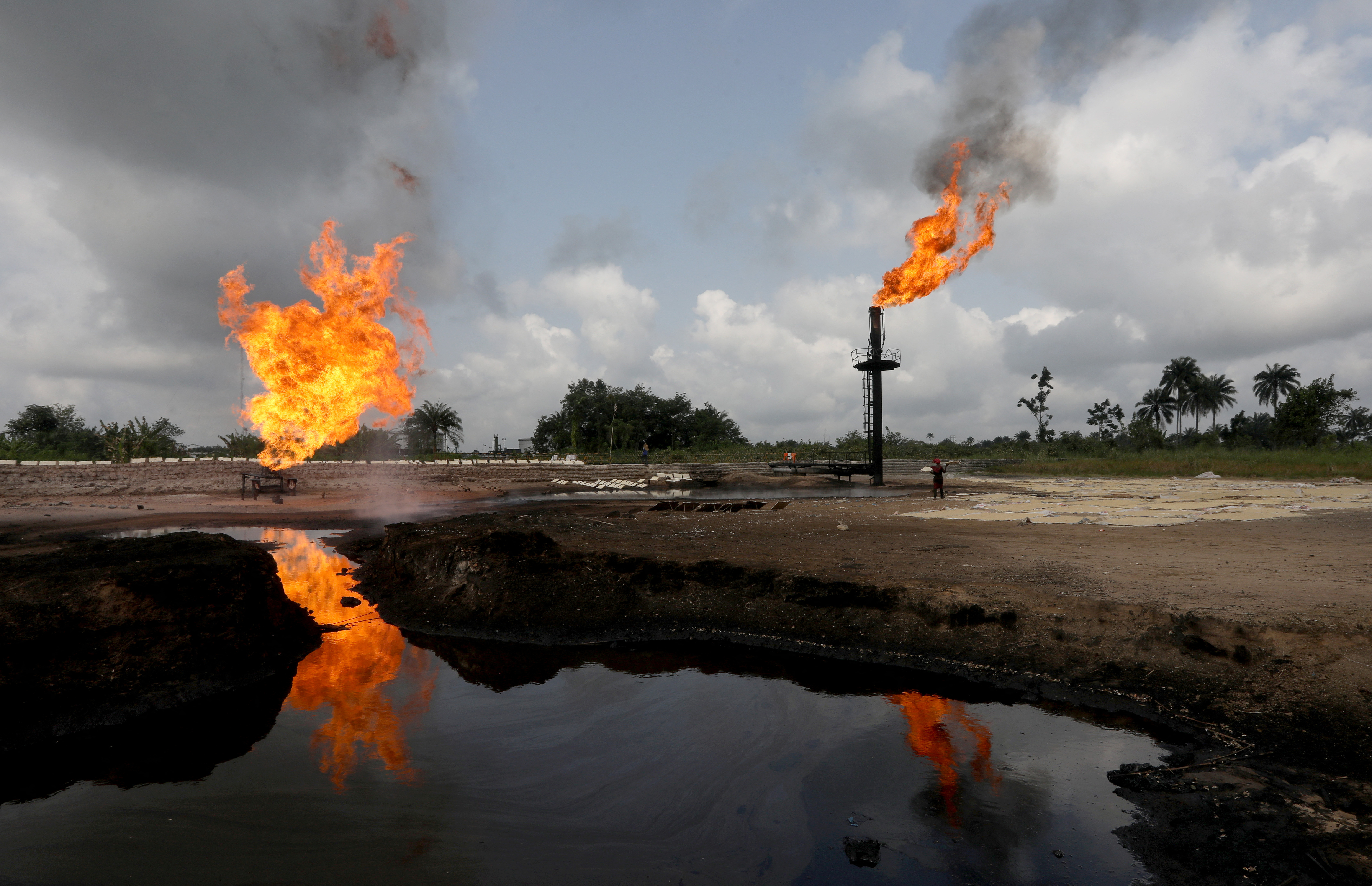 A reflection of two gas flaring furnaces is seen in the pool of oil-smeared water at a flow station in Ughelli, Delta State