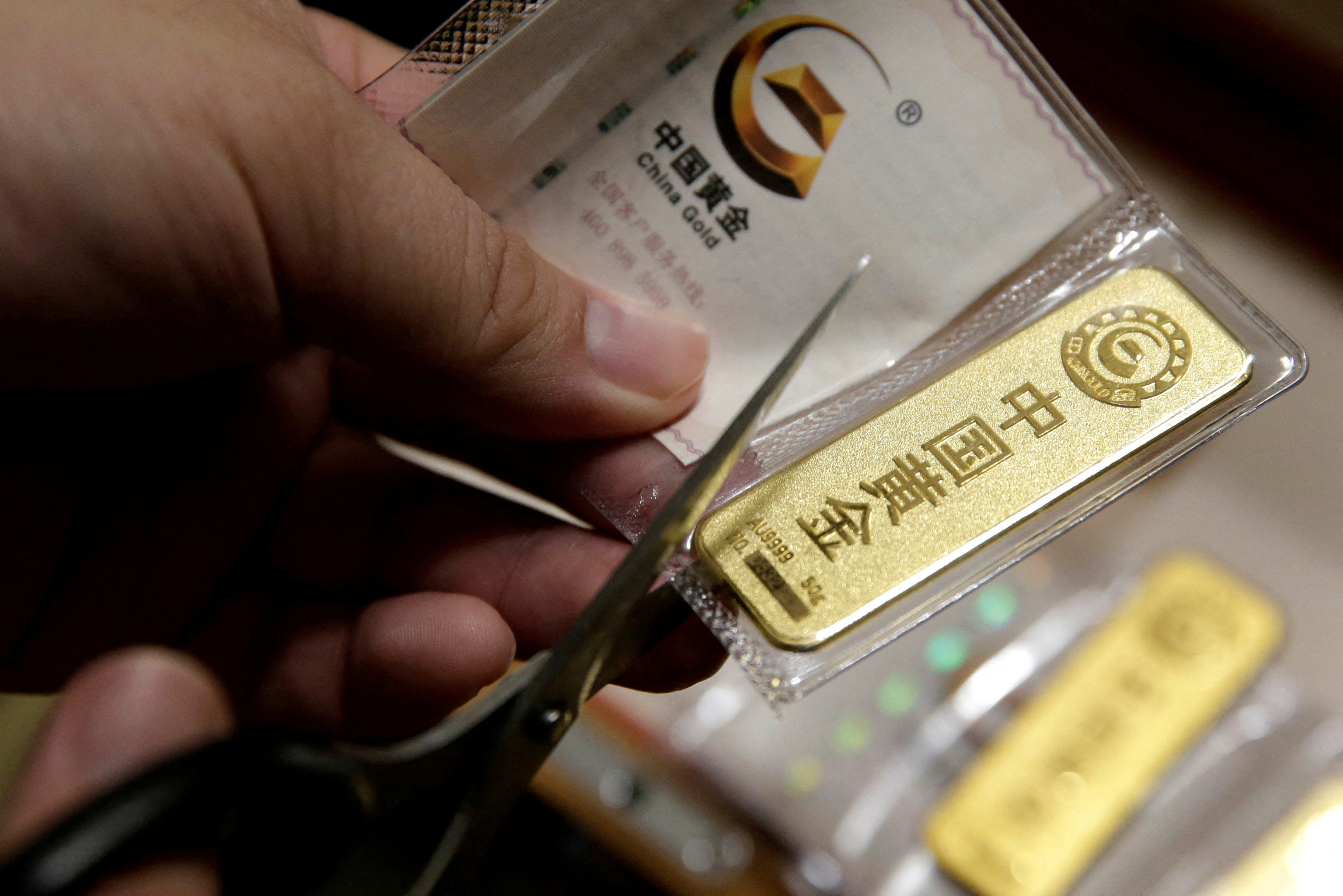A man cuts open the bag after he bought 50 gram gold bars as an investment in Beijing