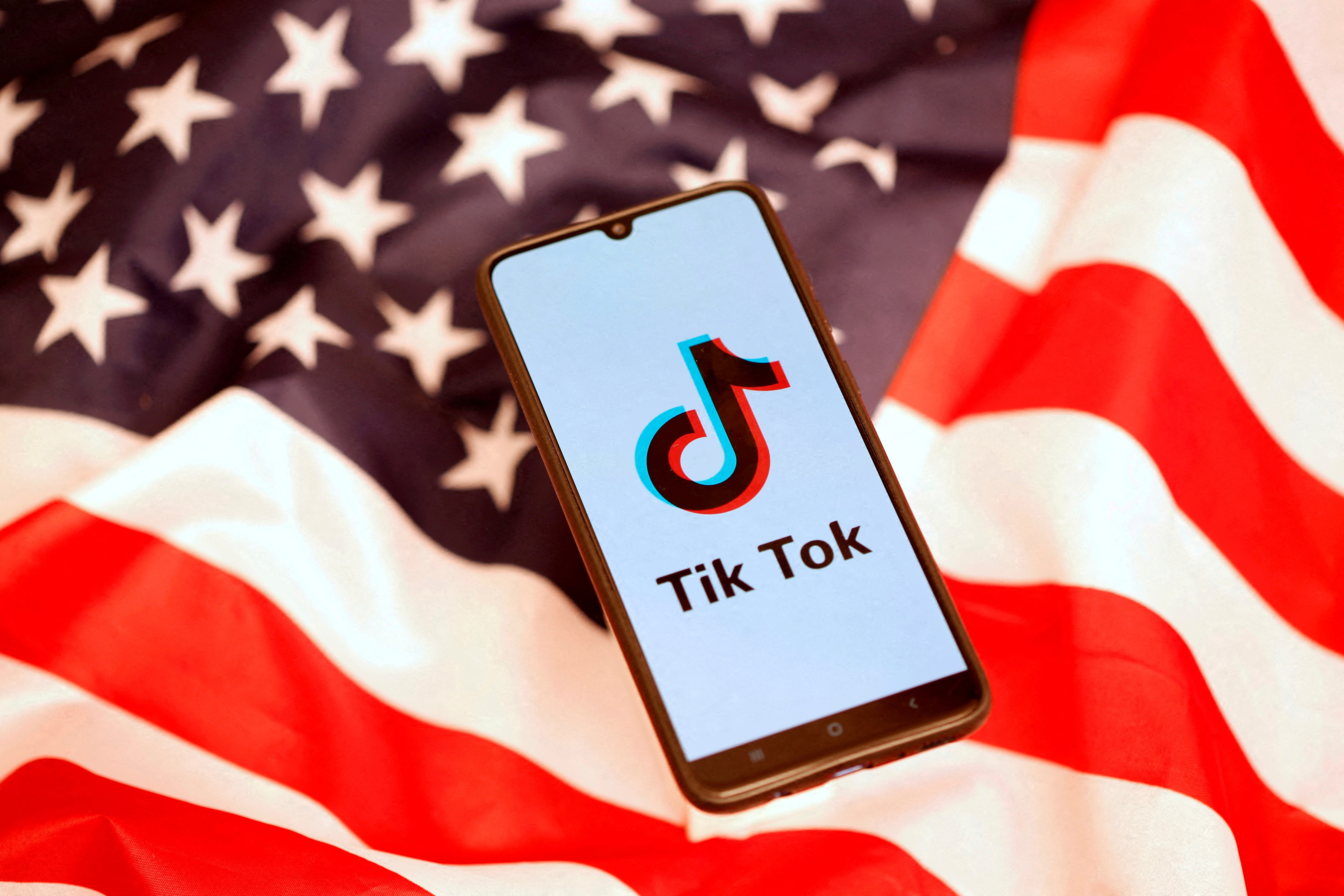 El logotipo de TikTok se muestra en el teléfono inteligente encima de la bandera de EE. UU. en esta ilustración