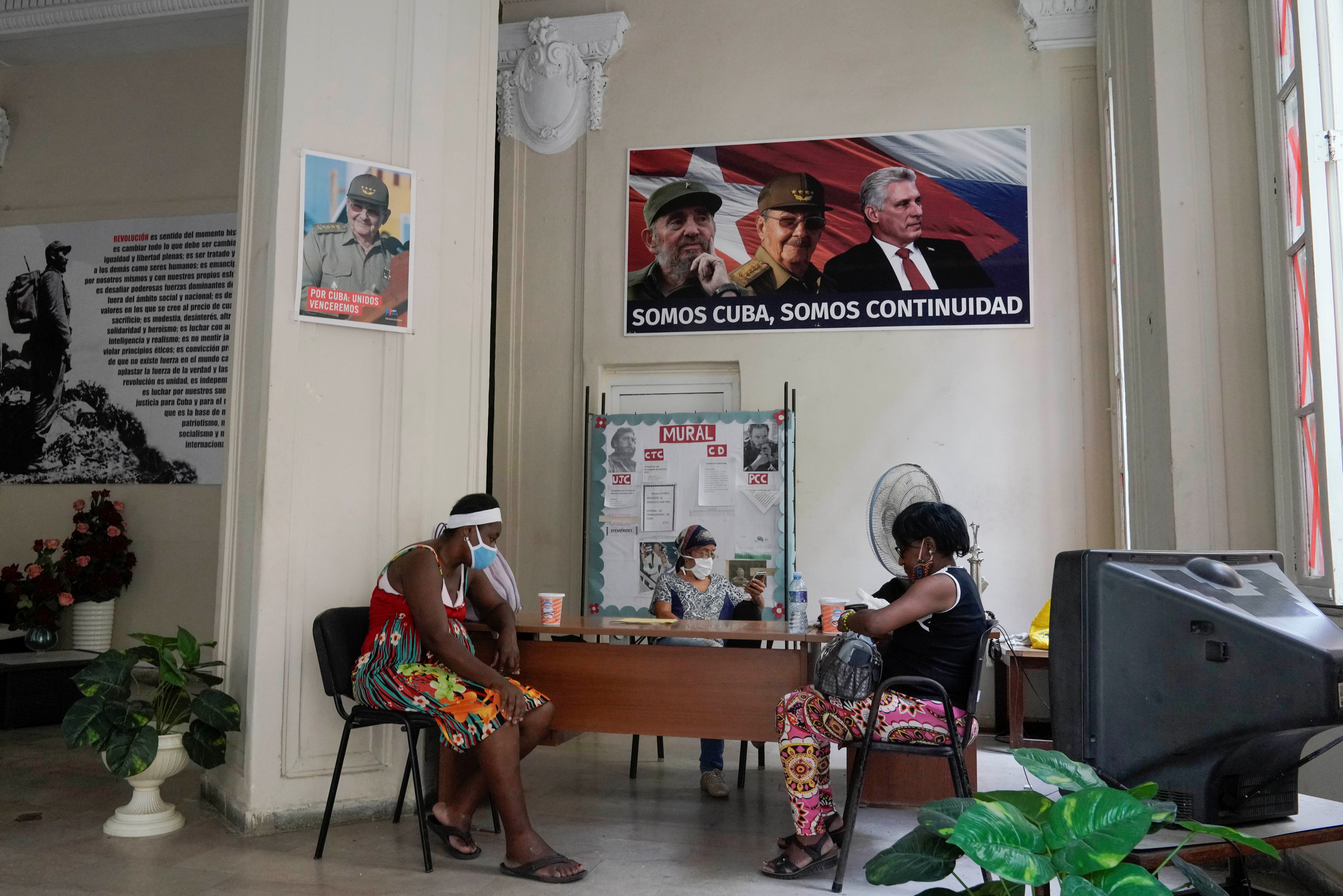 People sit under a poster with images of Fidel Castro, Raul Castro and Miguel Diaz-Canel in Havana