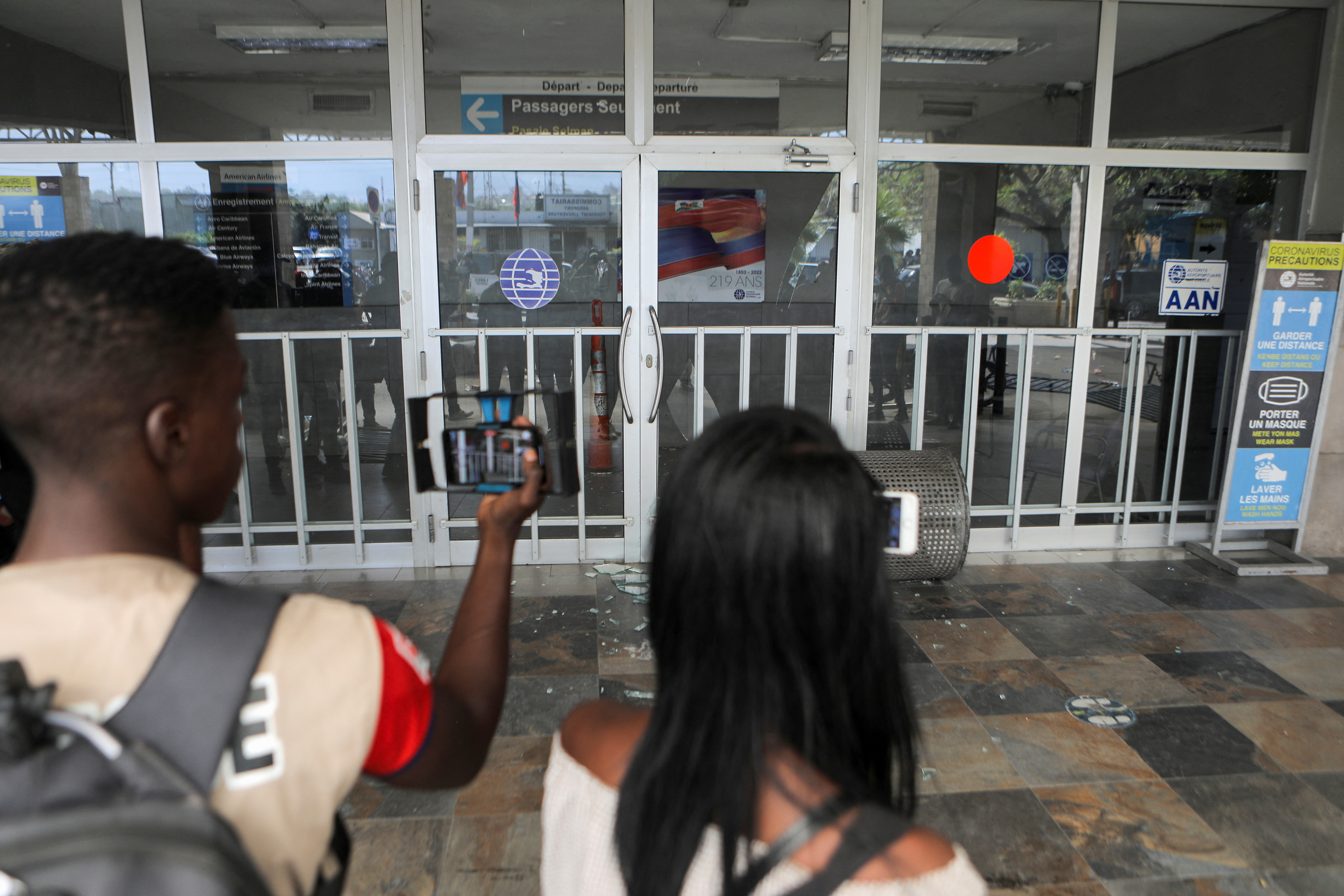 Reporters record with their phones the damage left by demonstrators after breaking into the Toussaint Louverture International Airport, in Port-au-Prince