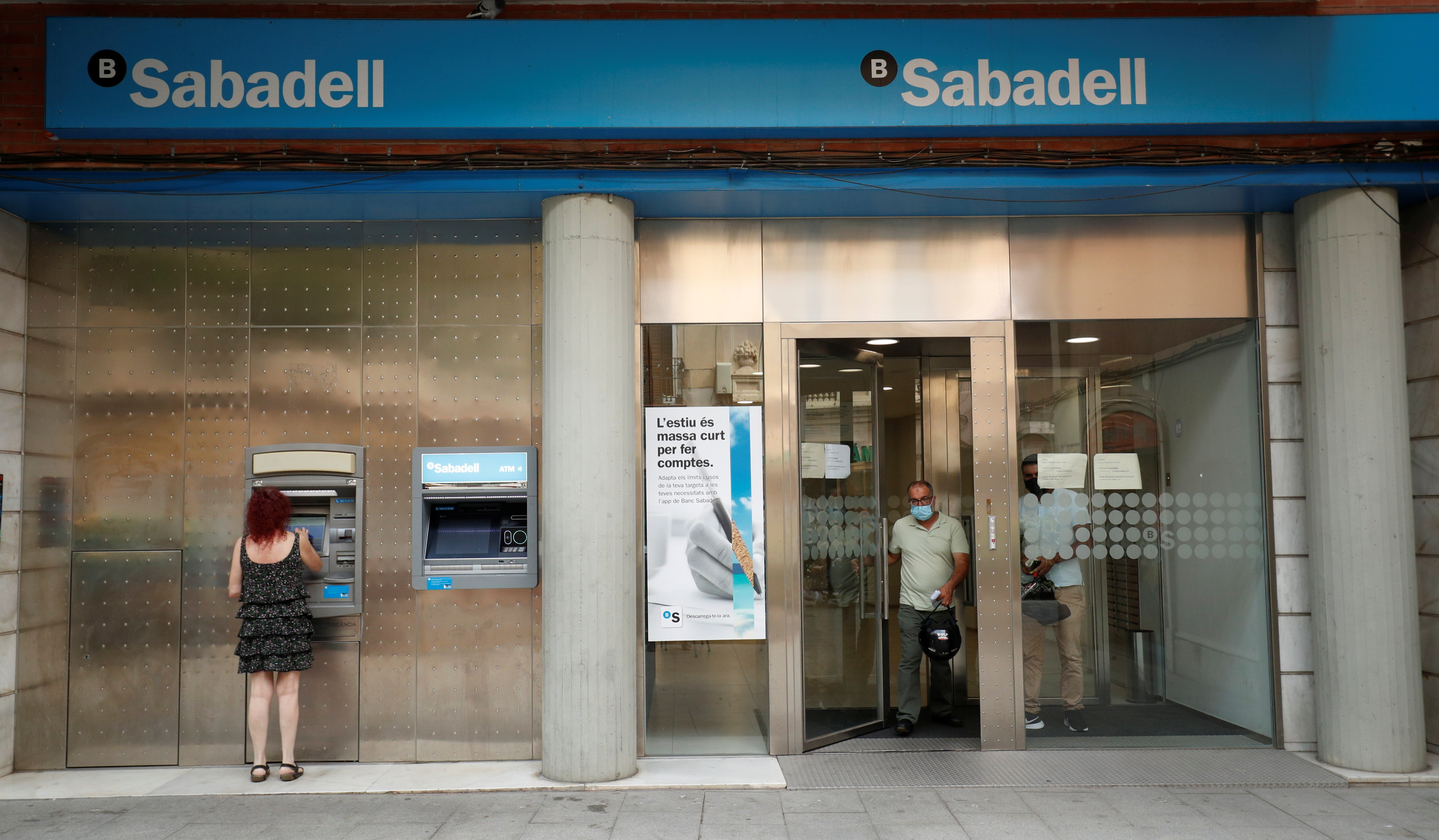 A woman uses an ATM machine as people leave a Sabadell bank office in Barcelona