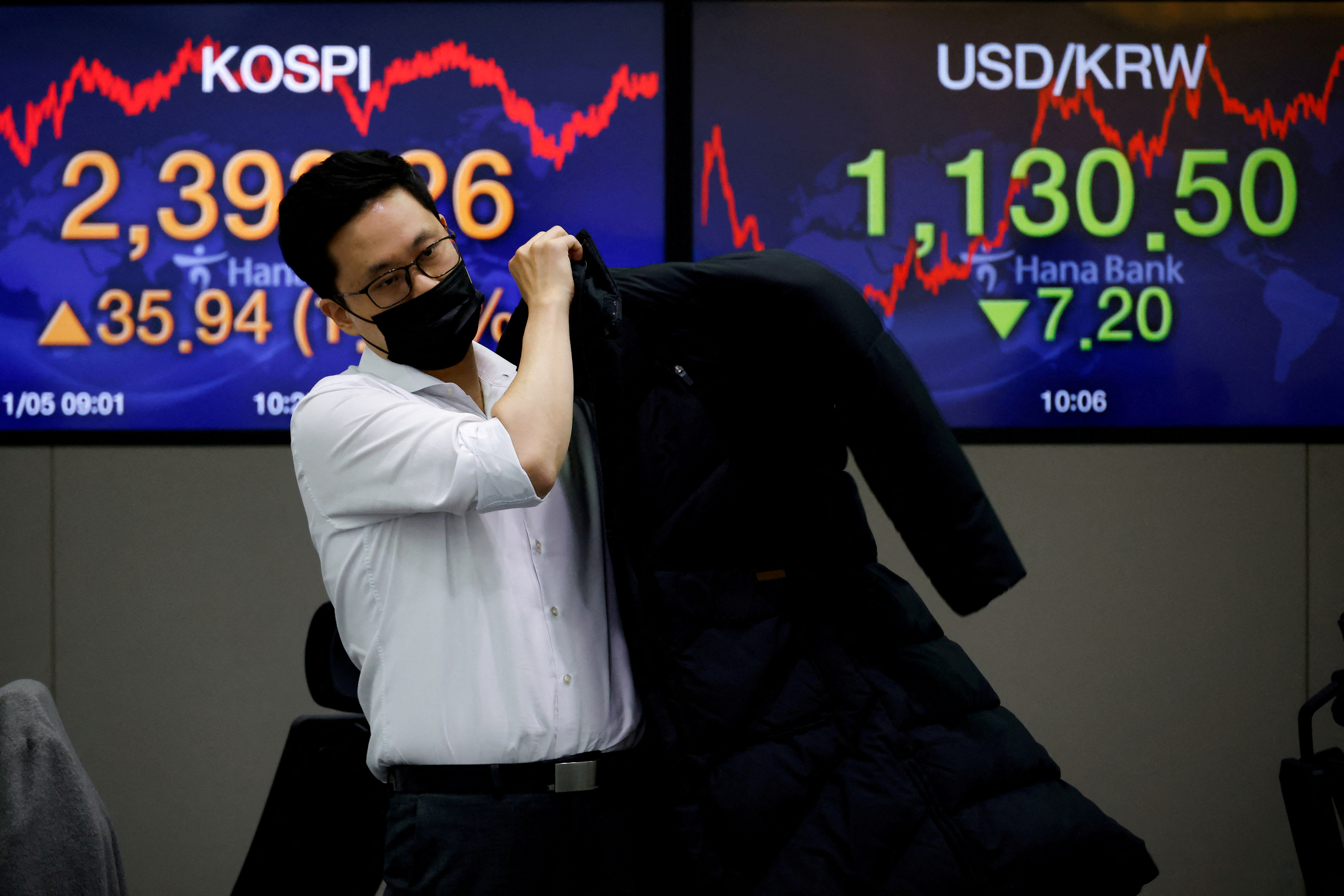 A currency dealer walks past electronic boards showing the Korea Composite Stock Price Index (KOSPI) and the exchange rate between the U.S. dollar and South Korean won at a dealing room of a bank, in Seoul