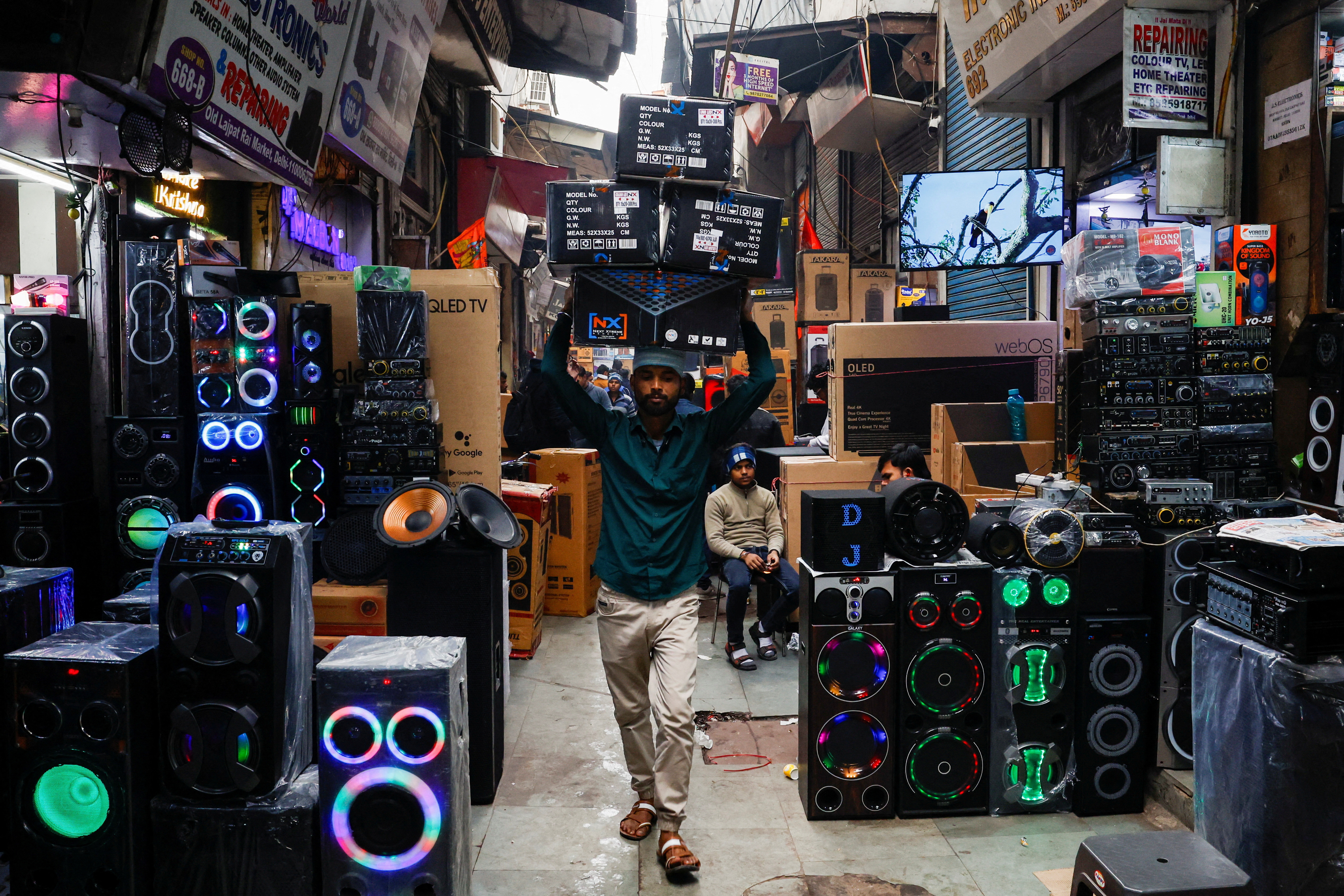 A labourer carries boxes past electronic gadgets on display at a wholesale market in the old quarters of Delhi