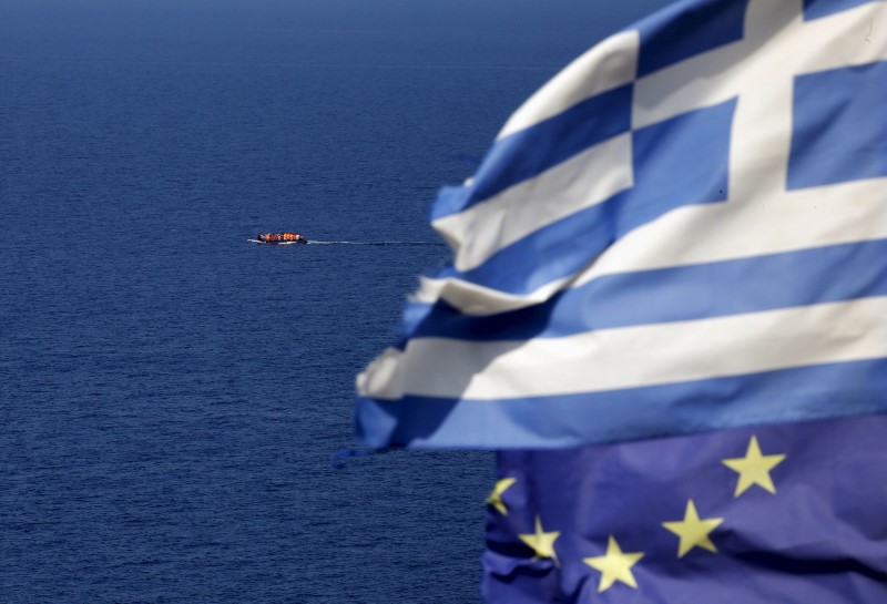 A dinghy overcrowded with migrants and refugees approaches the island of Lesbos as Greek and EU flags flutter atop a hill