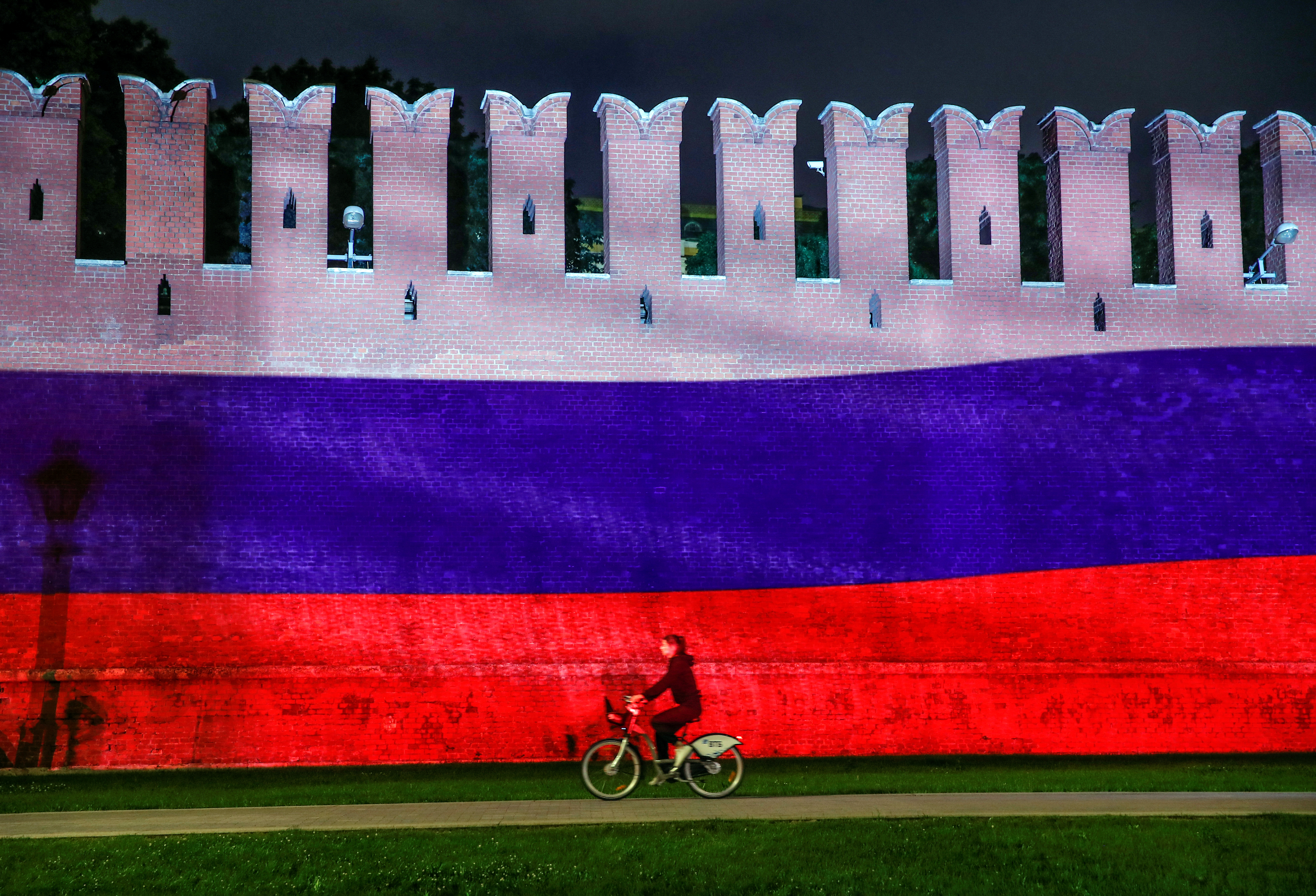 m_FILE PHOTO: A woman rides a bicycle past a part of the Kremlin wall where the Russian national flag is projected, during celebrations of Russia Day in Moscow
