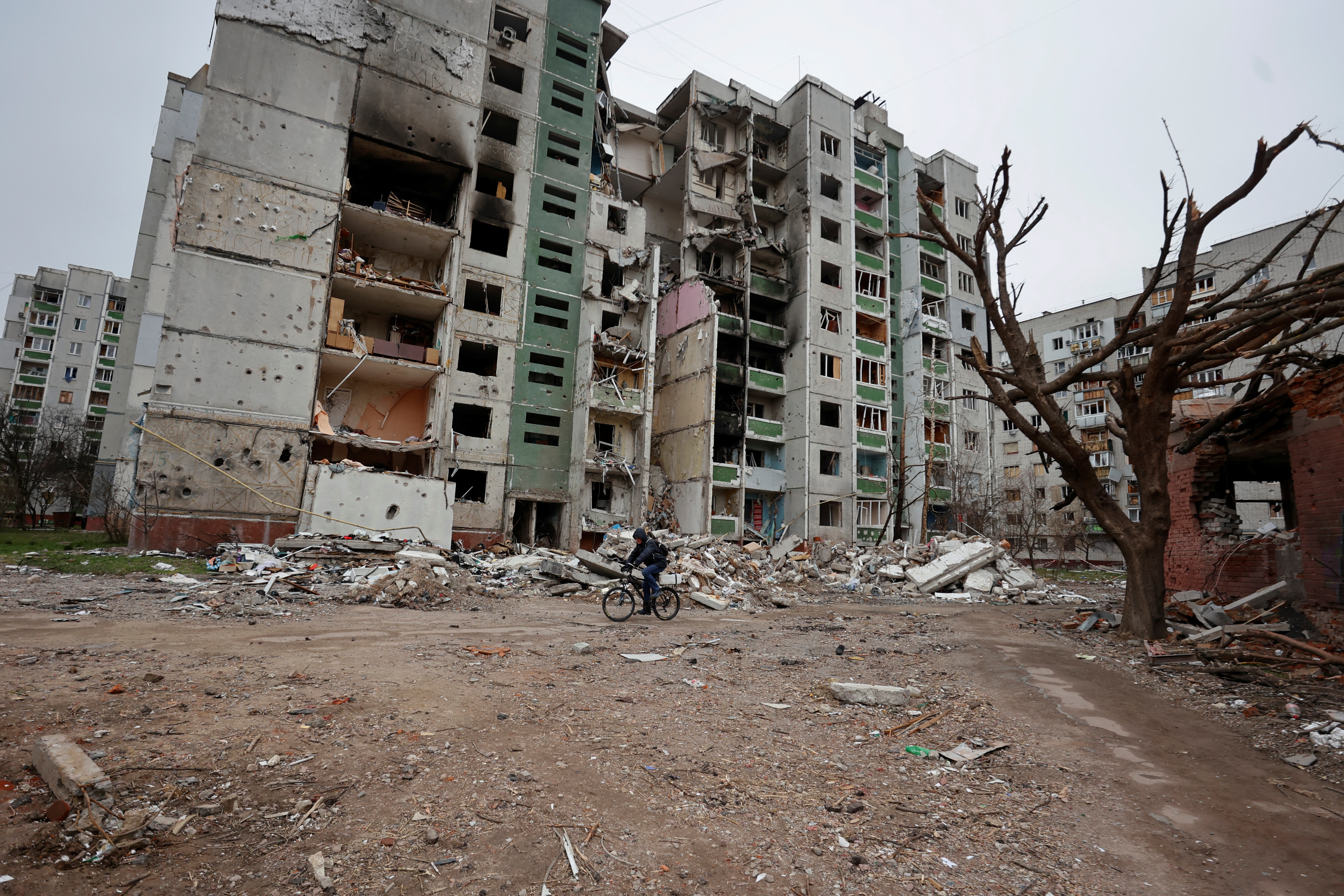 A local man rides a bicycle next to an apartment building damaged by heavy shelling in Chernihiv