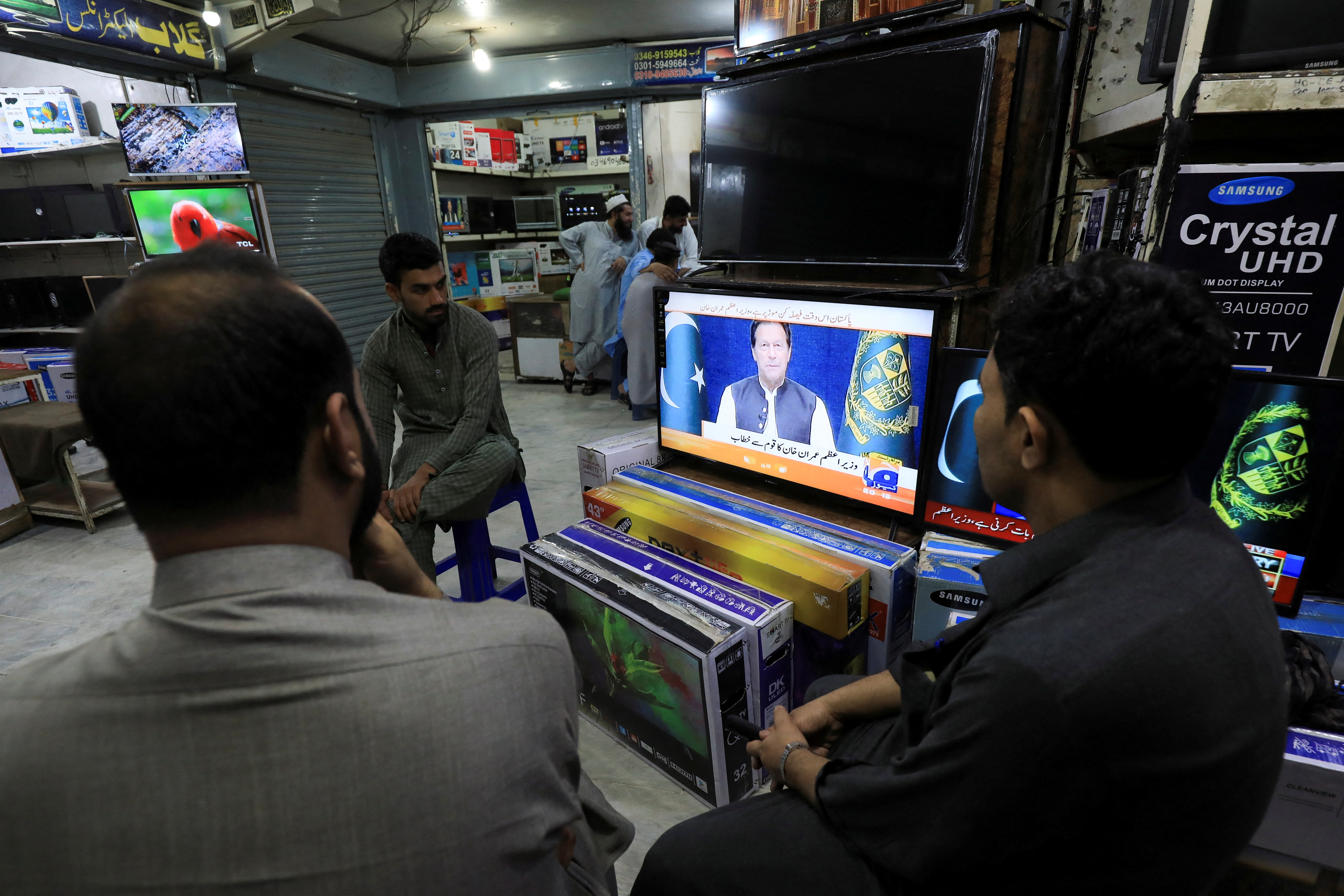 People watch the speech of Pakistani Prime Minister Imran Khan, at a shop in Peshawar,