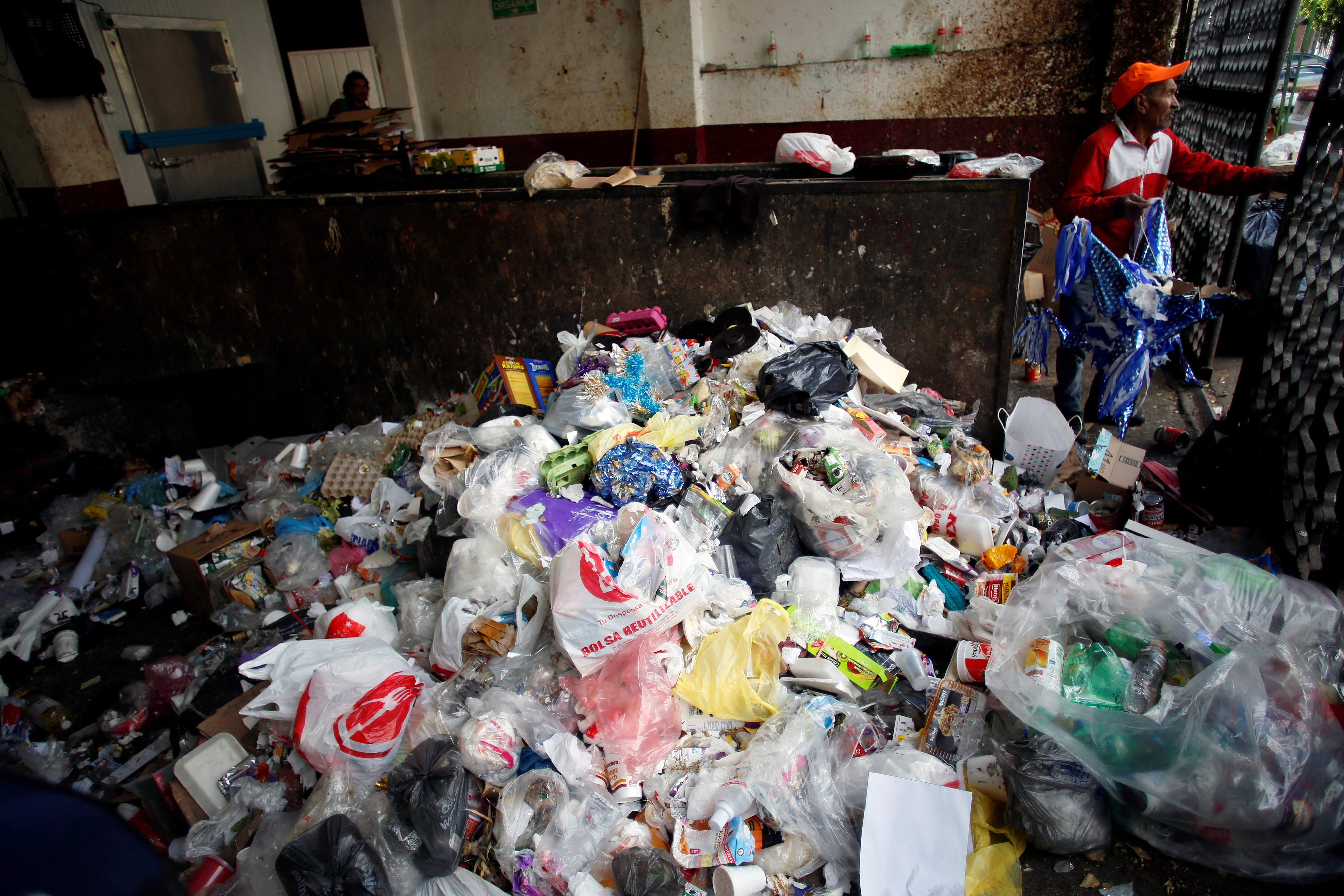 A man stands next to a pile of plastic garbage at a market which no longer provides plastic bags for customers to carry products, in Mexico City