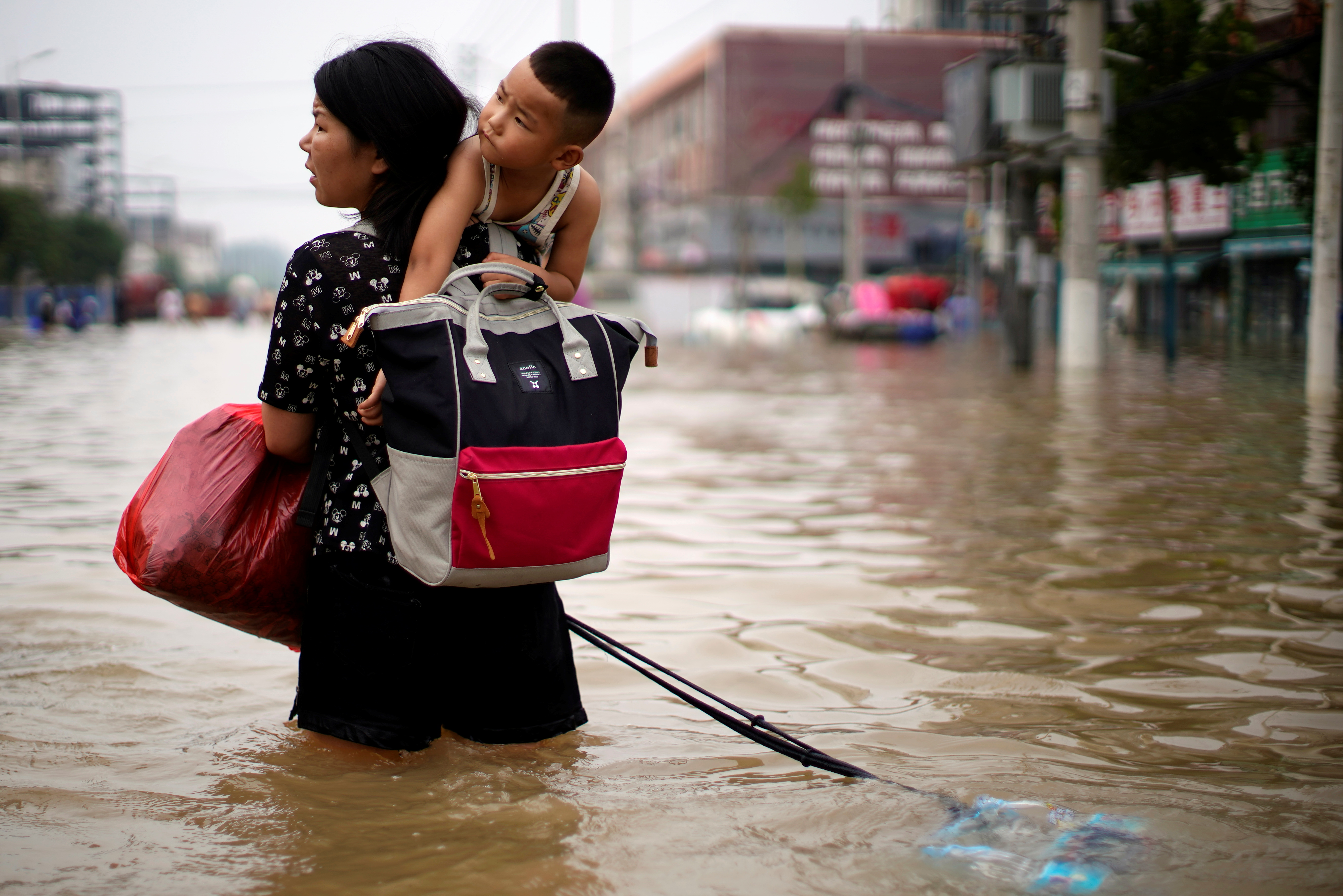 Woman carrying a child and belongings wades through floodwaters following heavy rainfall in Zhengzhou