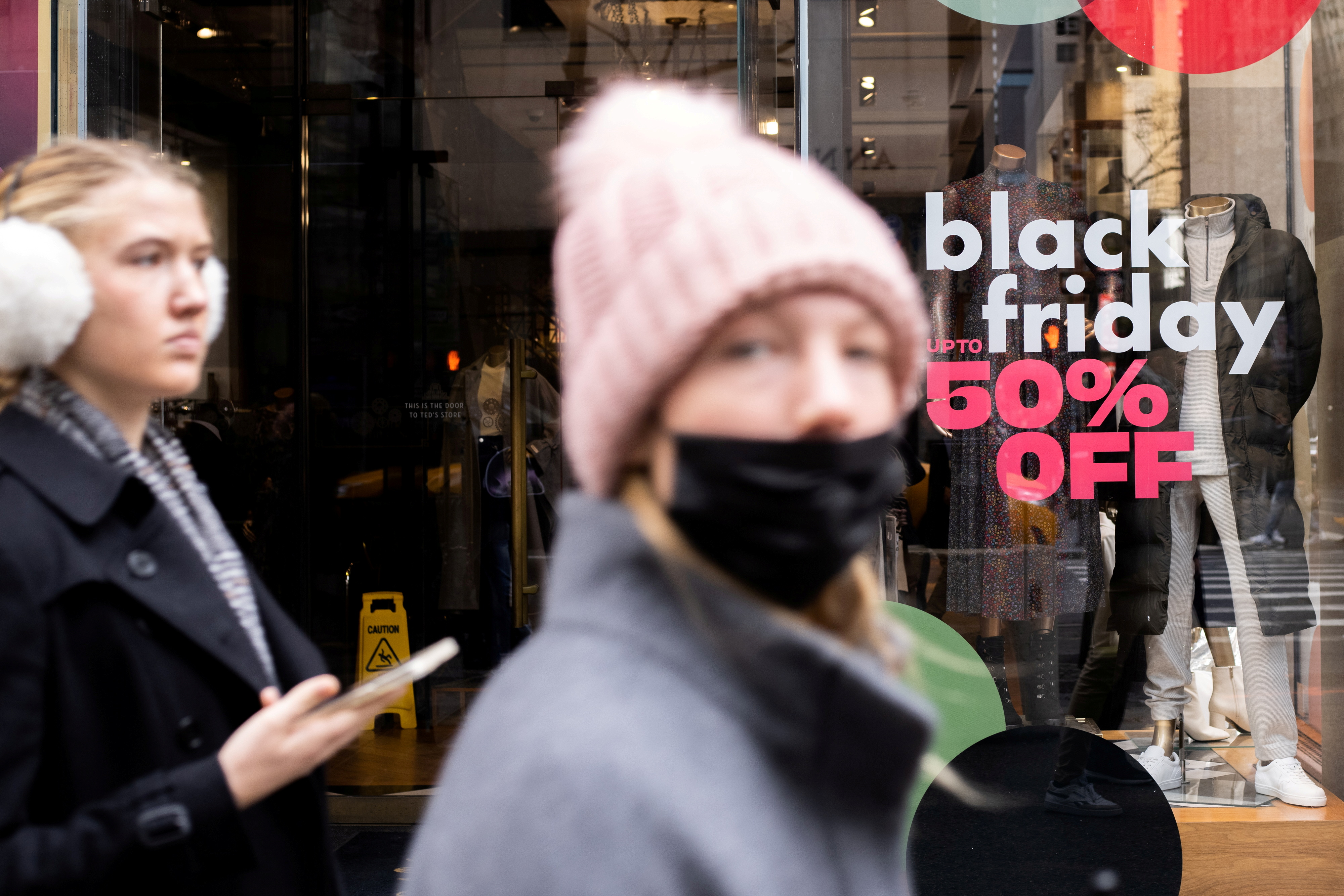 People walk along a store with sales signage during Black Friday sales in the Manhattan borough of New York City, New York, U.S., November 26, 2021. REUTERS/Jeenah Moon