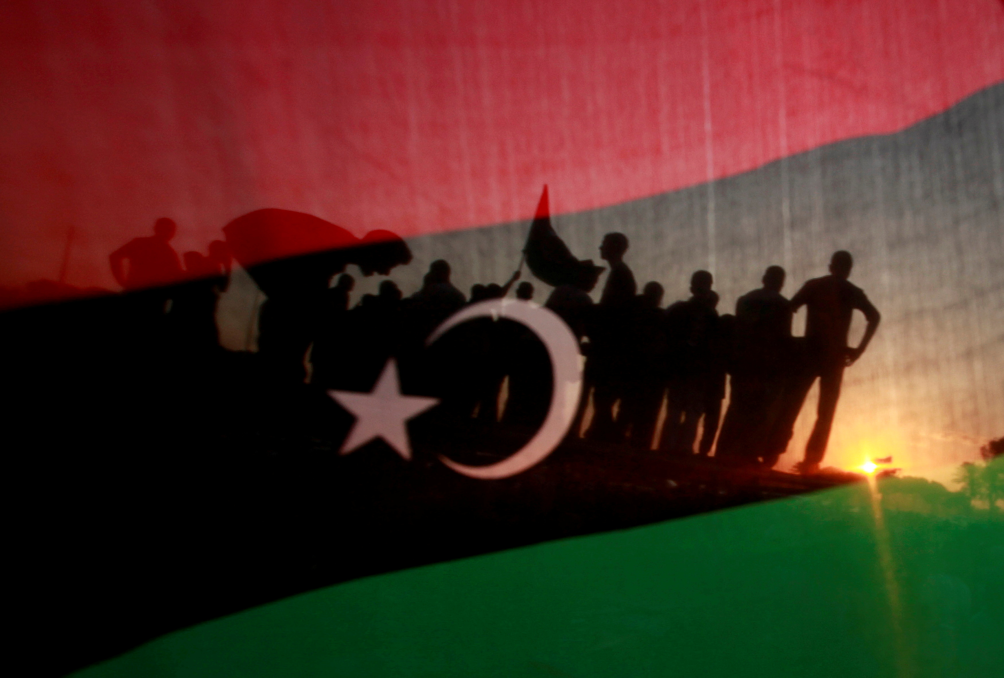 Libyans are seen through a Kingdom of Libya flag during a celebration rally in front of the residence of Muammar Gaddafi at the Bab al-Aziziyah complex in Tripoli September 13, 2011. REUTERS/Suhaib Salem/File Photo