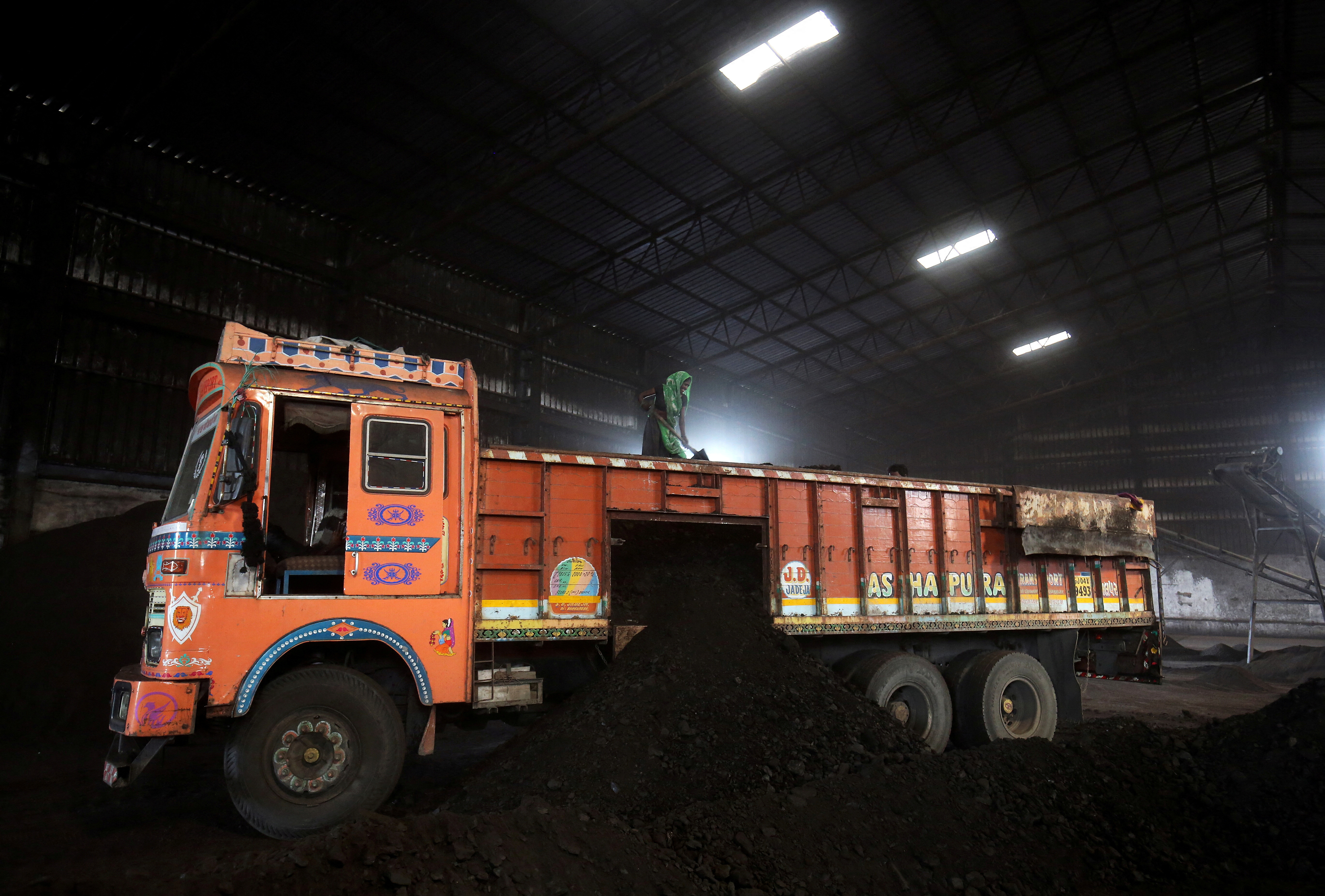 Worker shovels coal in a supply truck at a yard on the outskirts of Ahmedabad
