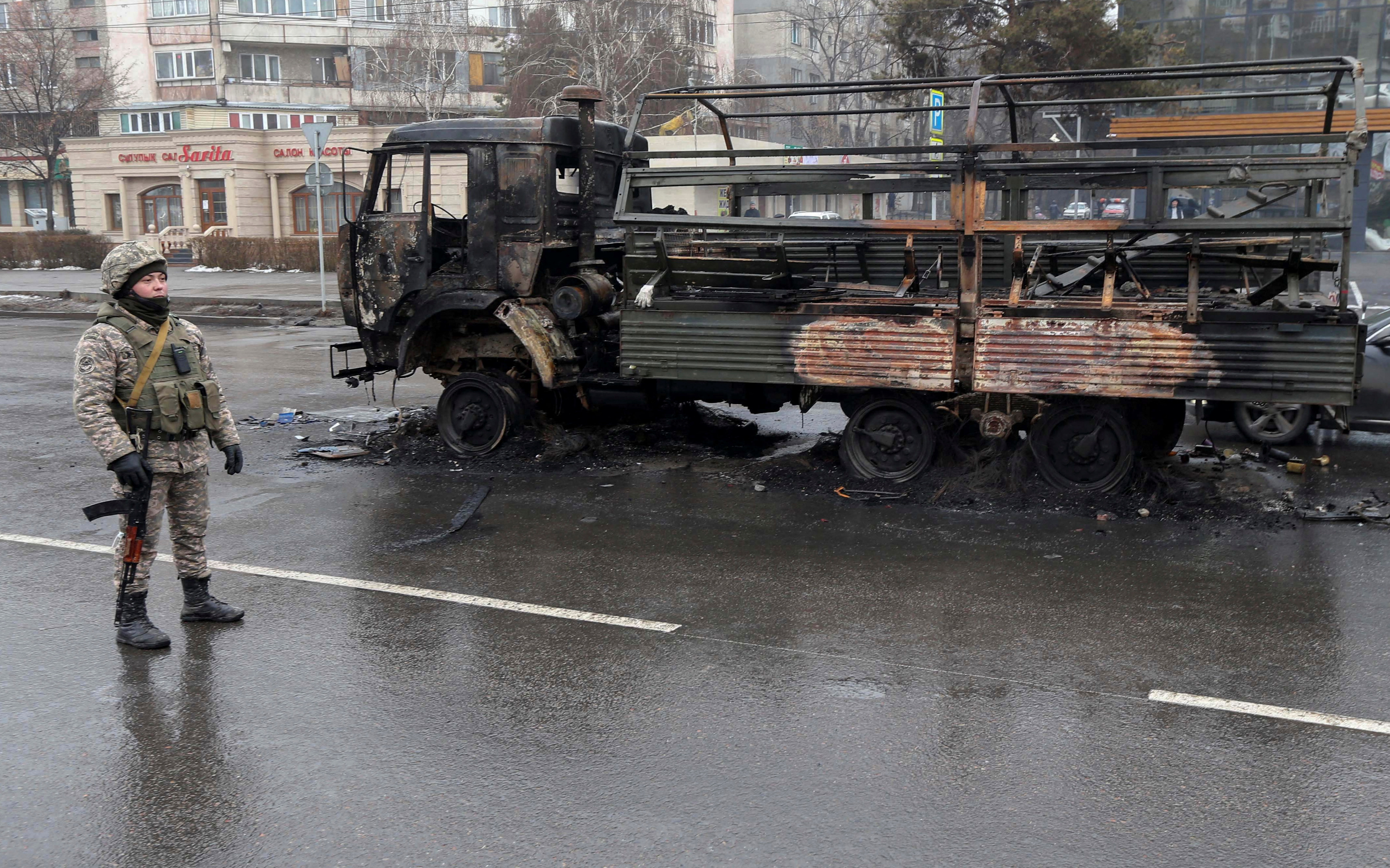A Kazakh law enforcement officer stands guard near a burnt truck while checking vehicles in a street following mass protests triggered by fuel price increase in Almaty, Kazakhstan January 8, 2022. REUTERS/Pavel Mikheyev