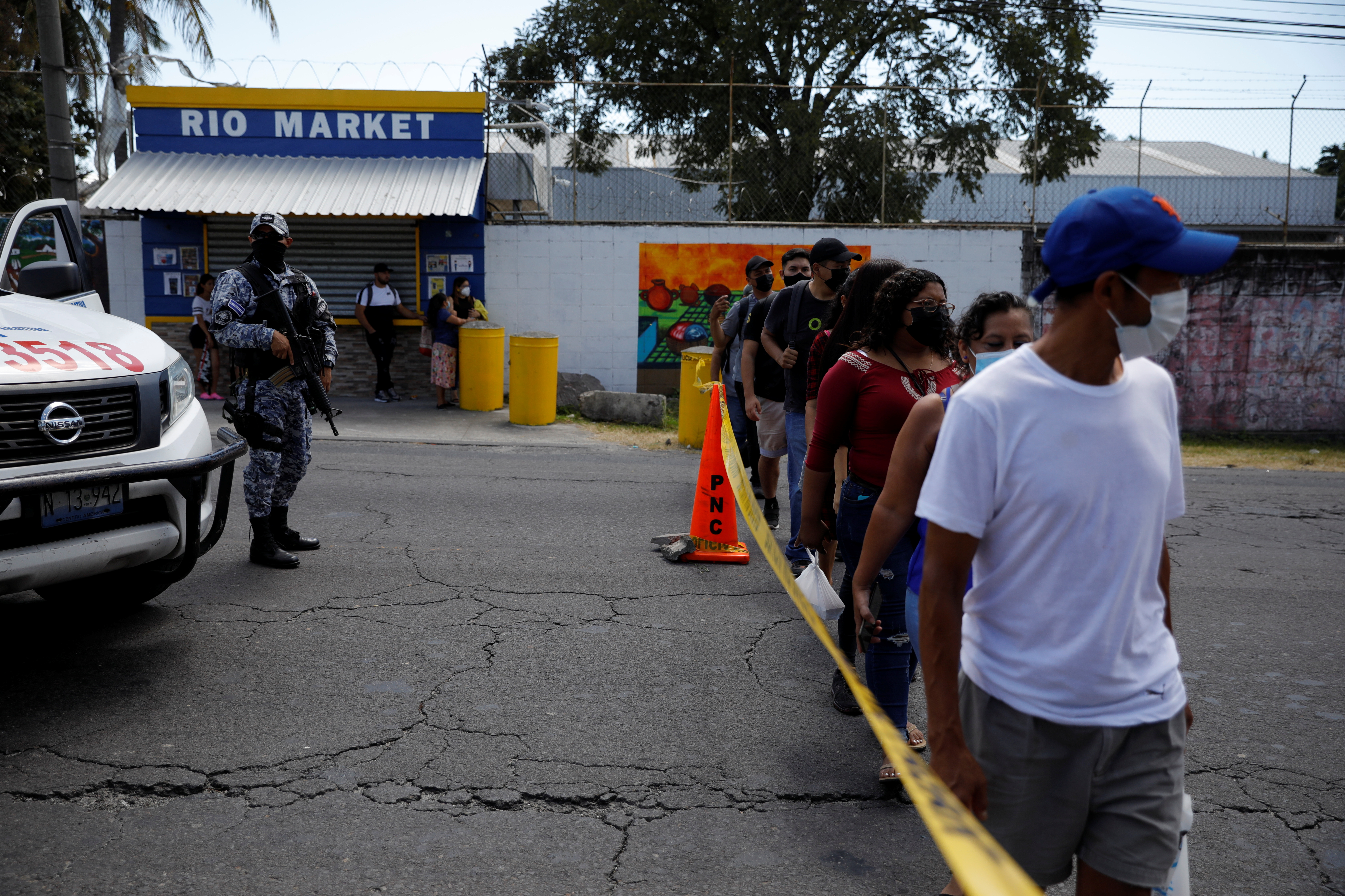 People cross by a crime scene where a man was killed inside a car, as Salvadoran President Nayib Bukele deploys military to patrol the streets throughout the country in response to a sharp surge in murders this week, in San Martin, El Salvador November 11, 2021. REUTERS/Jose Cabezas