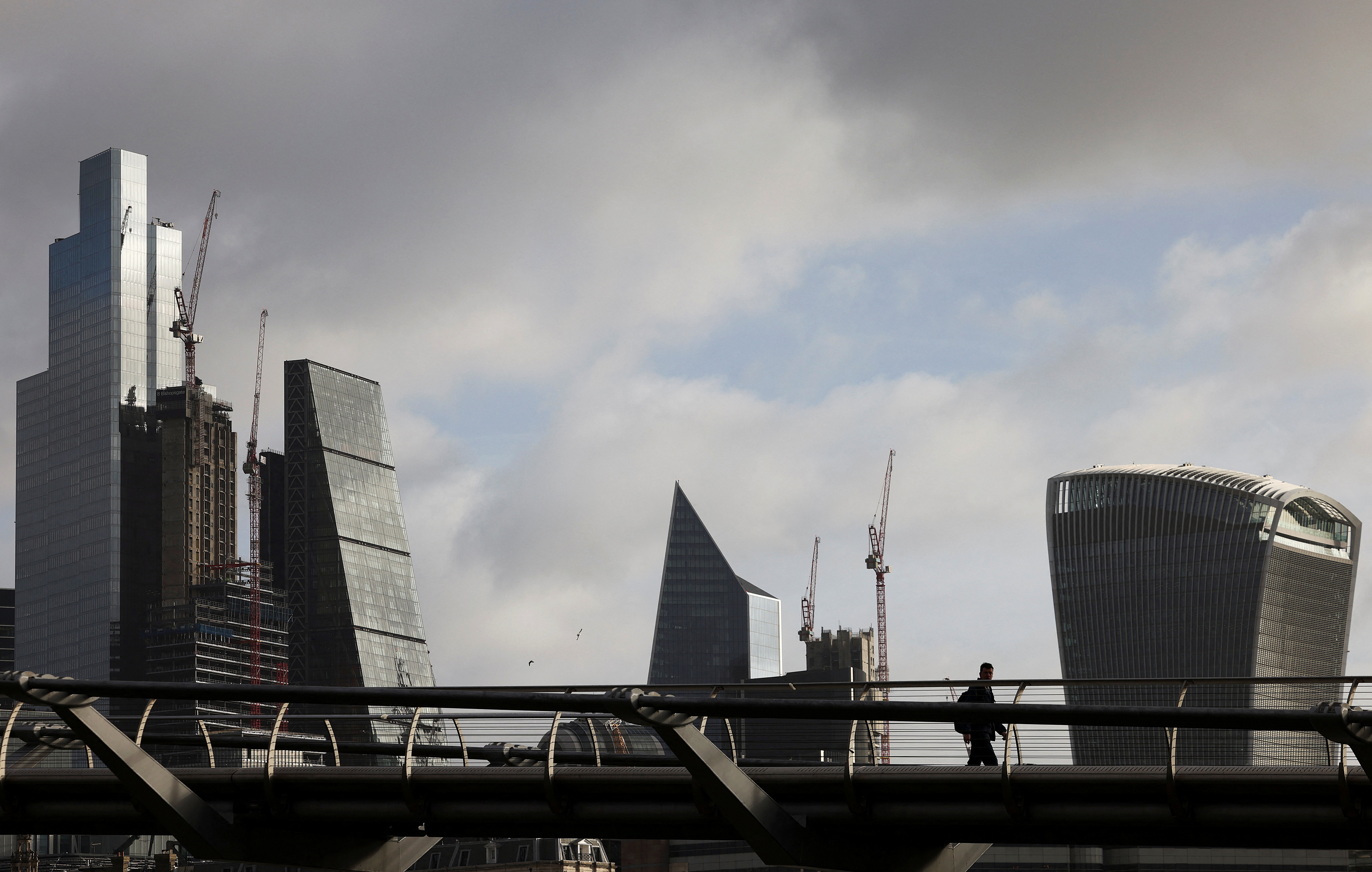 The City of London financial district is seen as people walk over Millennium Bridge in London