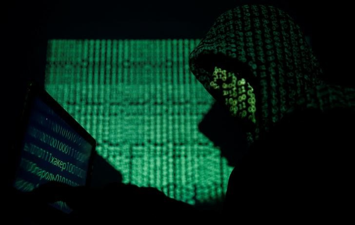 Hooded man holds a laptop computer as cyber code is projected on him in this illustration picture