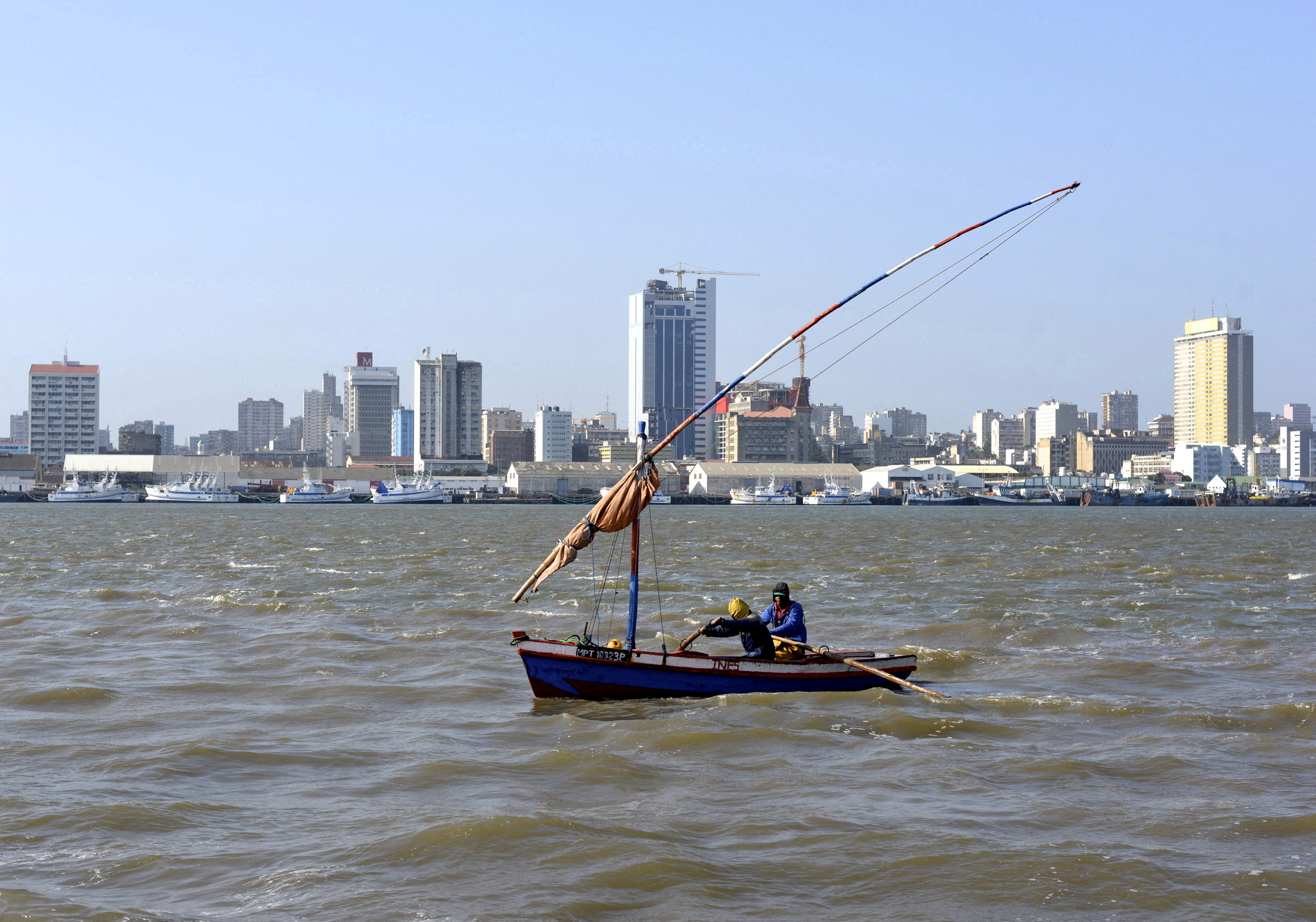 Traditional fishing boats sail as Mozambique's tuna fleet sits in dock beneath Maputo's skyline