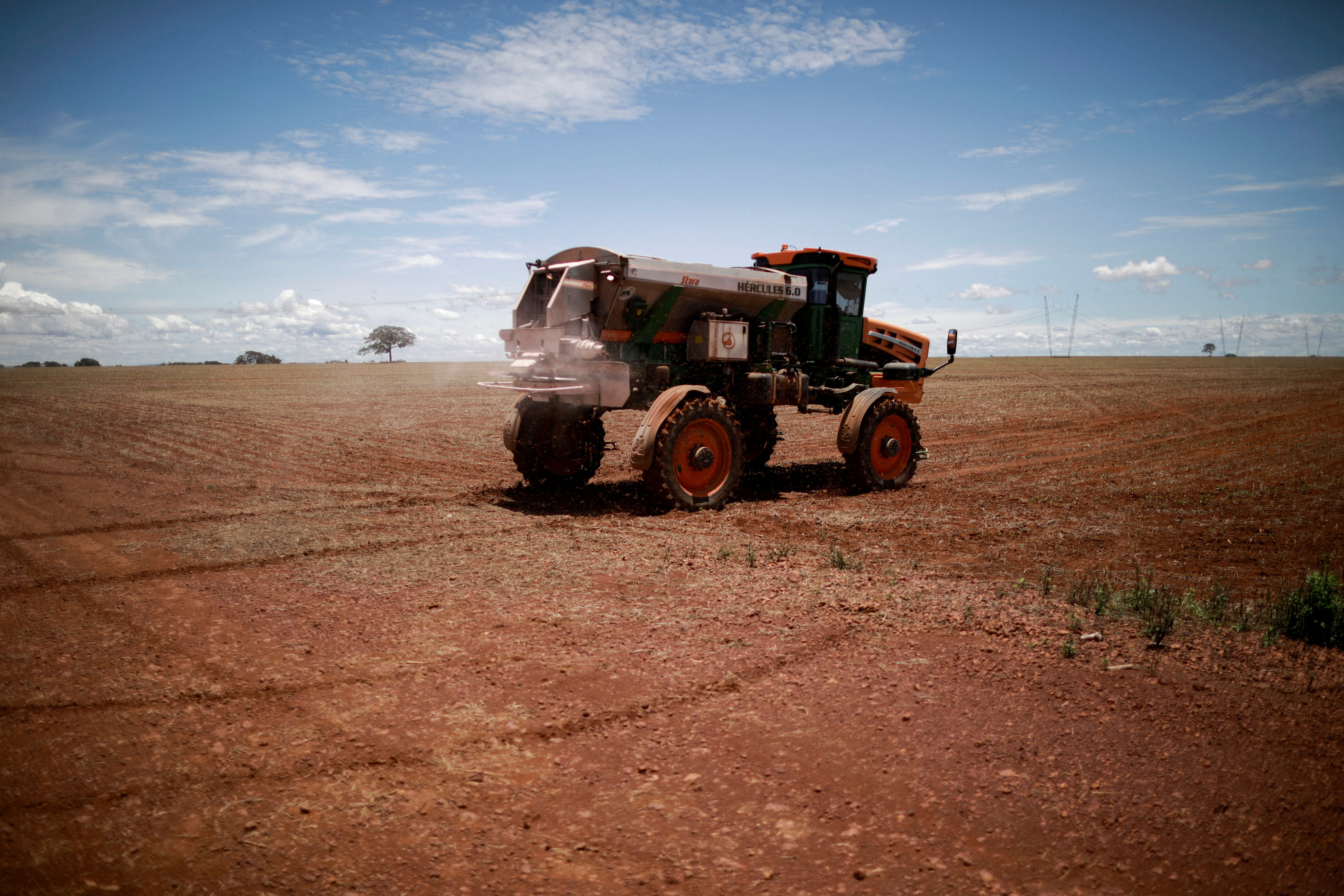 An agricultural worker drives a tractor spreading fertilizer in a soybean field, near Brasilia