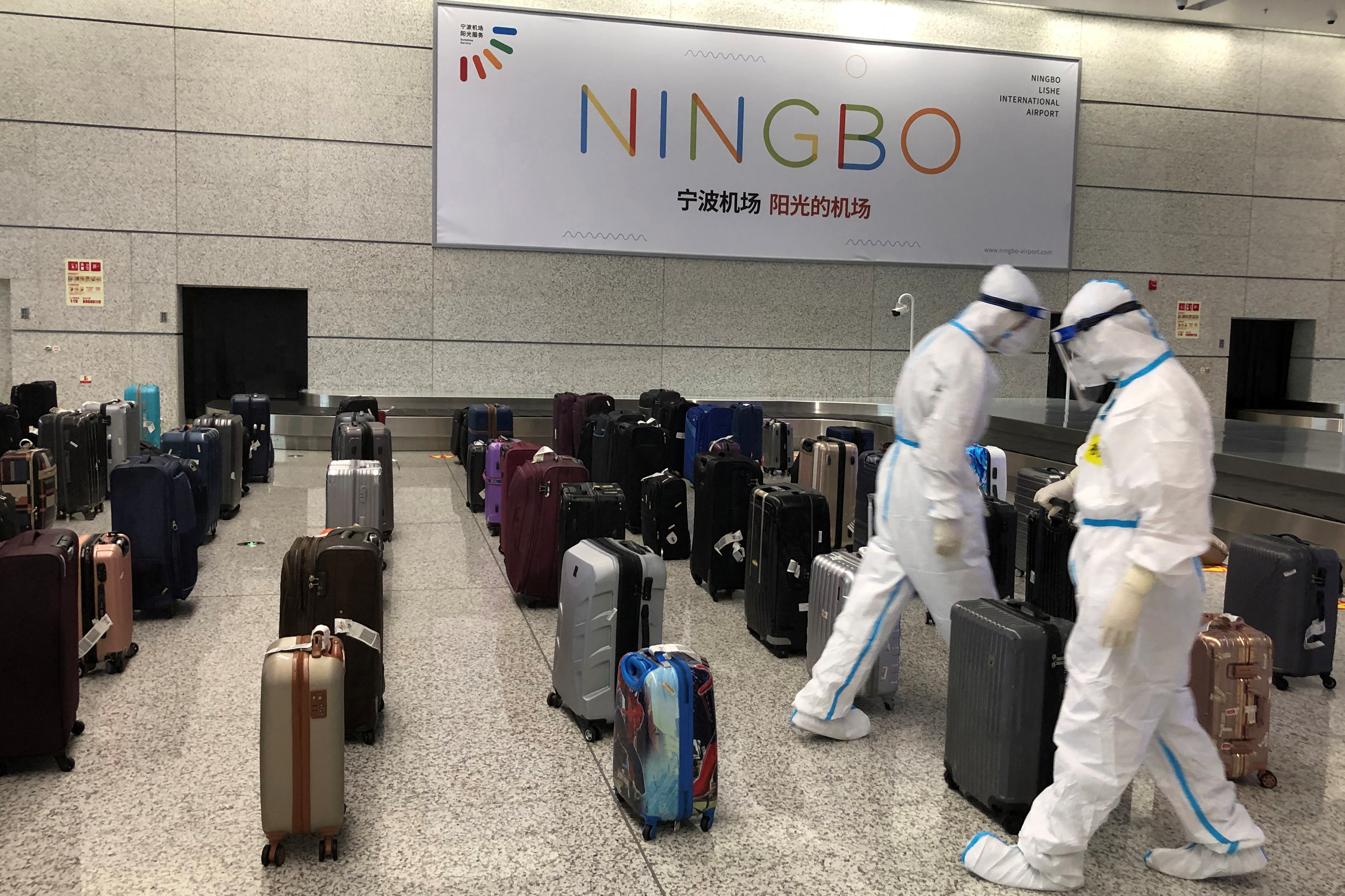 Workers in protective suits sort luggage arriving from New Delhi at Ningbo Lishe International Airport