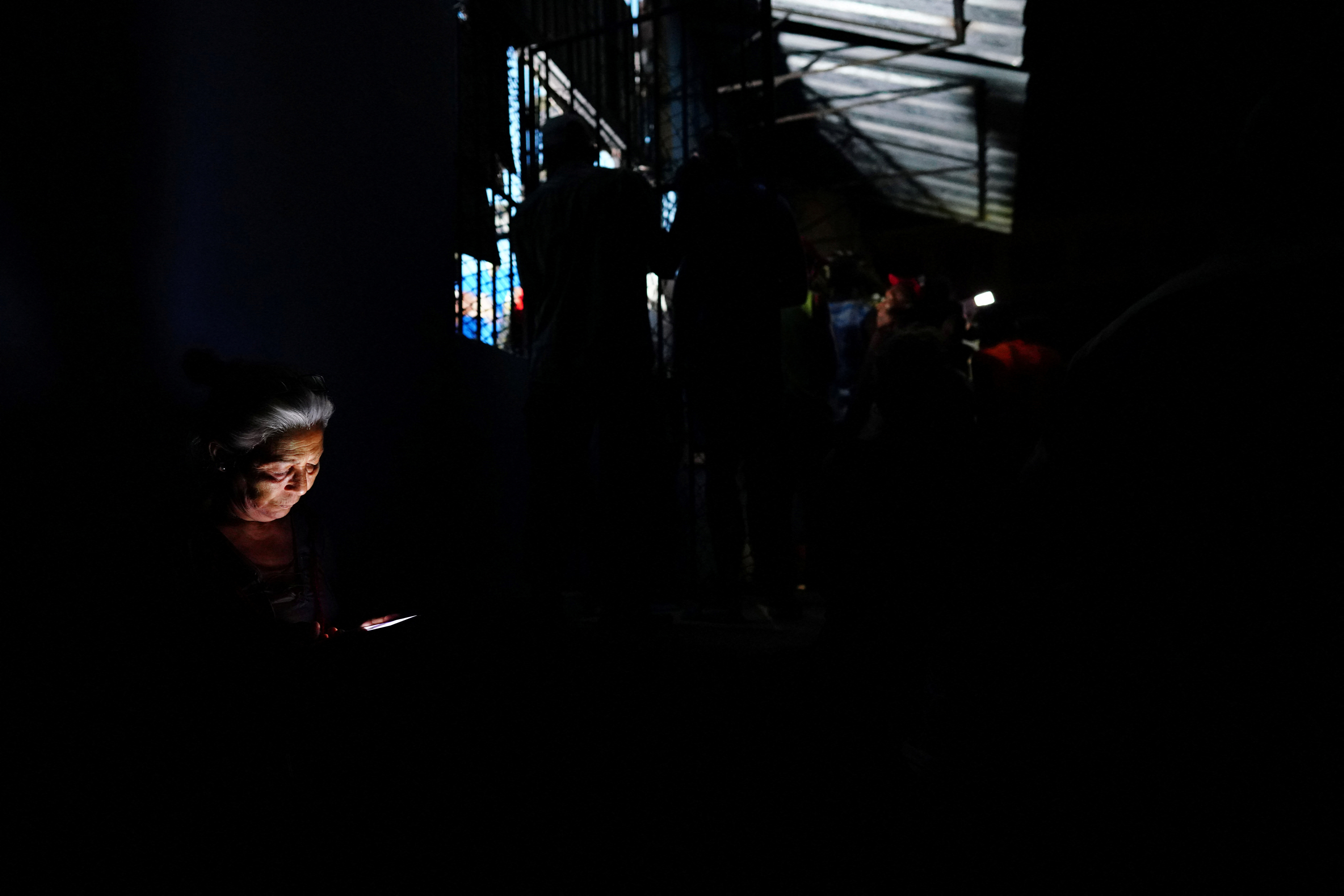 An elderly woman uses a mobile phone as she waits to get a once-monthly ration of chicken, during a blackout, at a small state-run market in Santiago